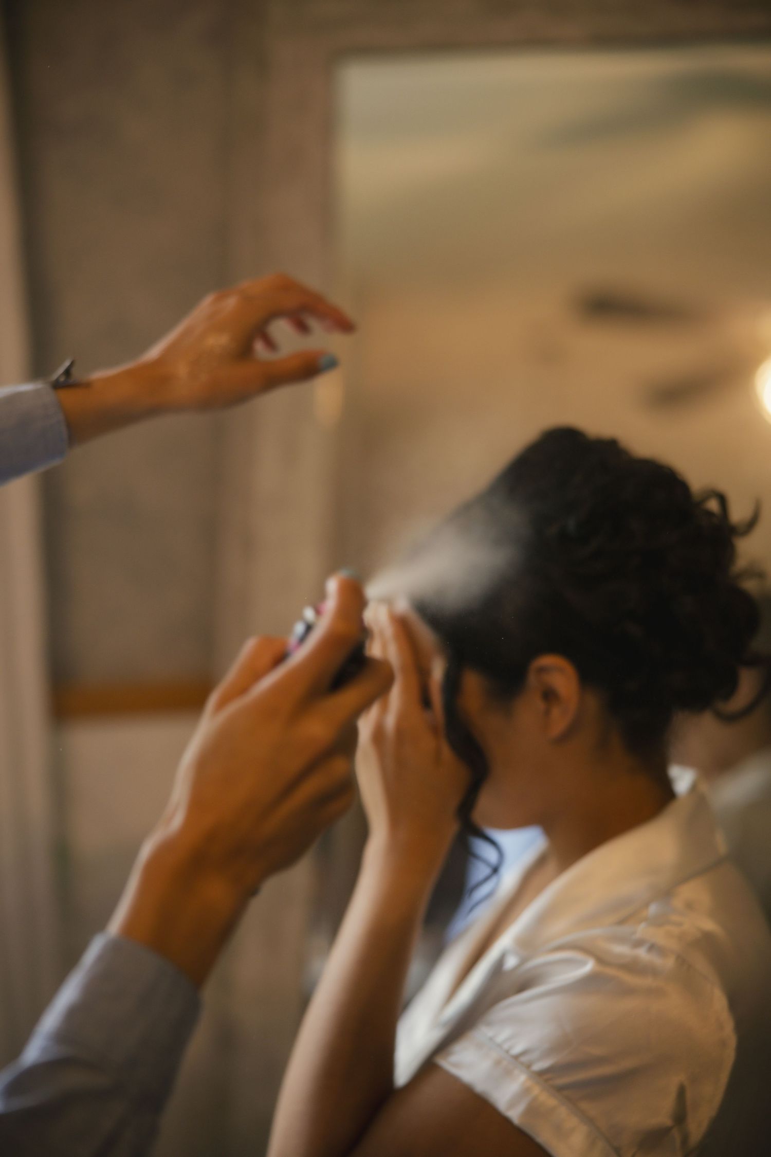 Someone getting hair spray applied during styling preparation in a dimly lit room.