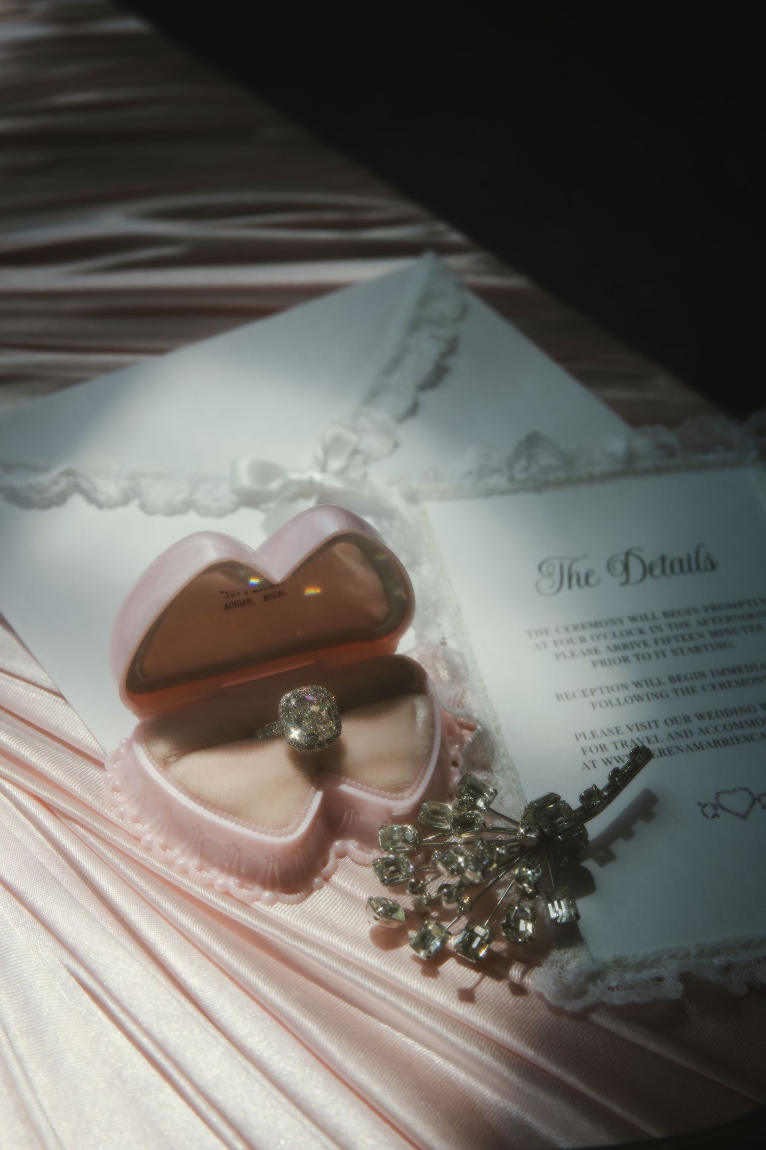 Pink satin ribbons and sparkling crystal embellishments arranged on a decorative paper surface.