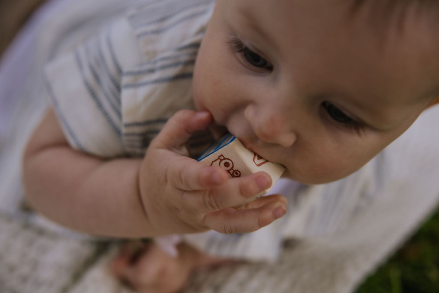 A small child holds a silver ring in their mouth while lying on the ground.
