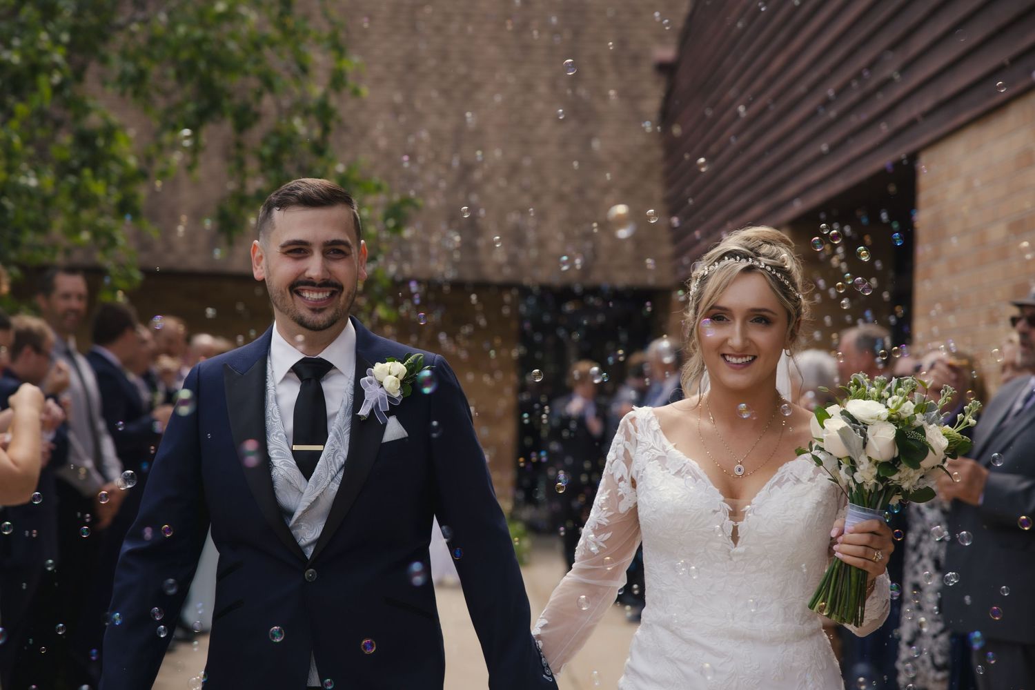 A bride and groom walk together smiling while guests shower them with confetti outside a venue.