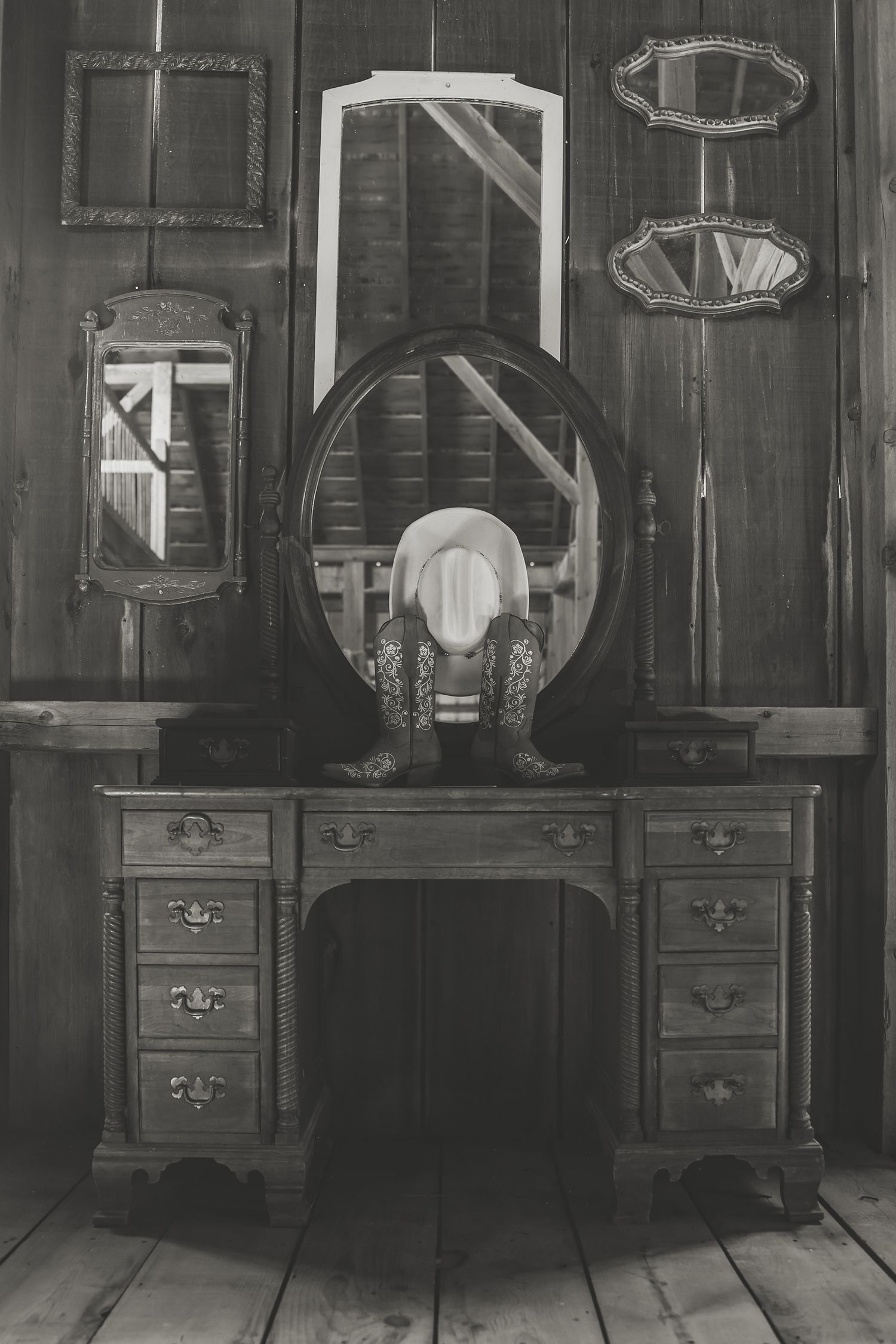 Antique dark wooden vanity with oval mirror and empty picture frames on wall in black and white photograph.