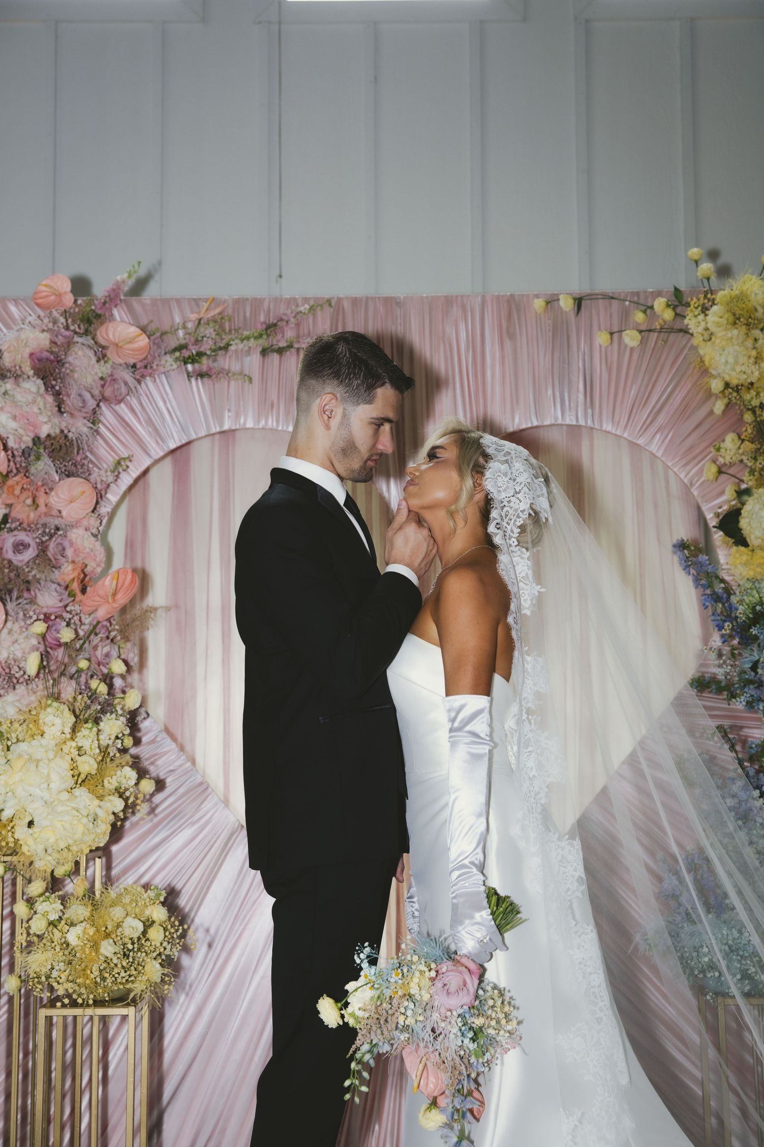 A romantic wedding moment captured in pink and floral decor as newlyweds share a kiss at their ceremony altar.