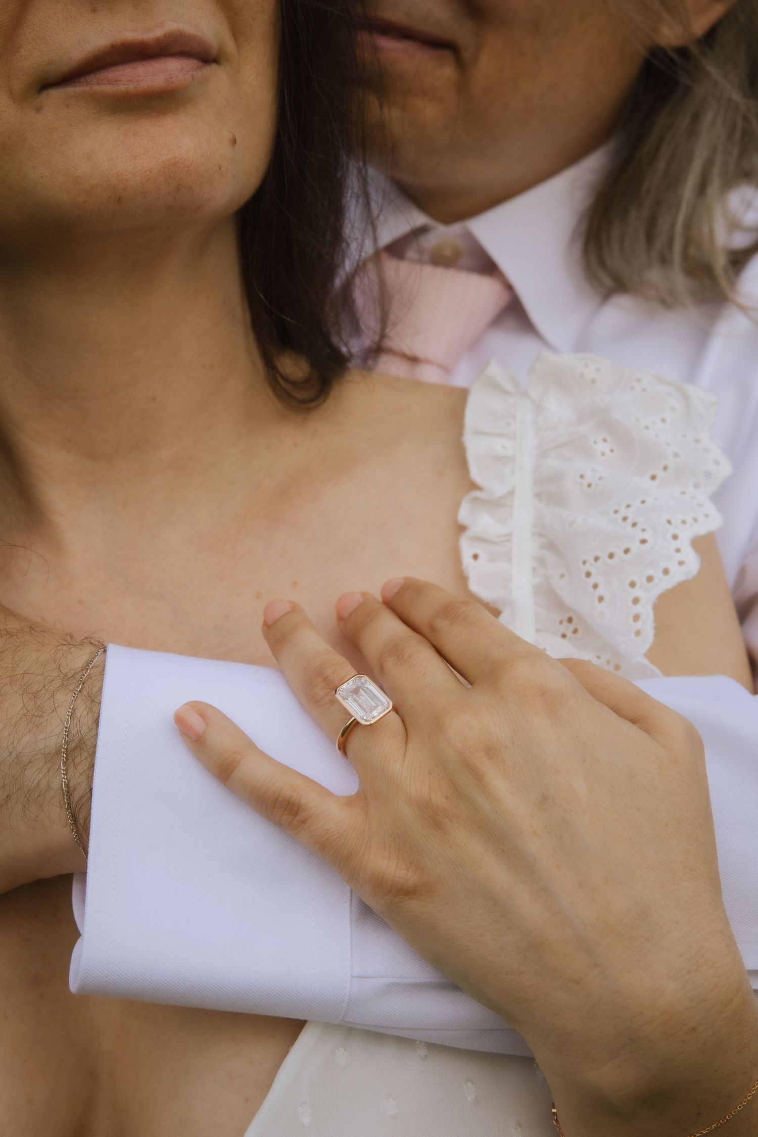 Close-up of an engagement ring on a hand resting against white fabric with delicate lace details.