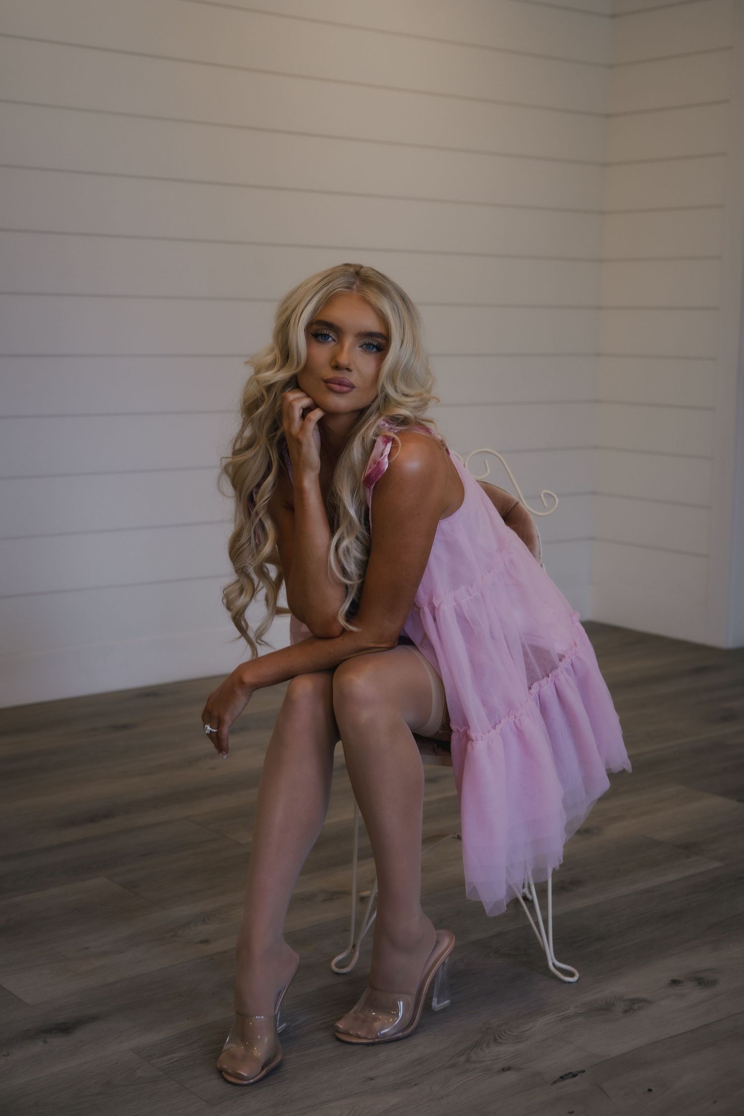 Multiple shots show someone in a pink dress and high heels posing on dark hardwood flooring against a white wall.