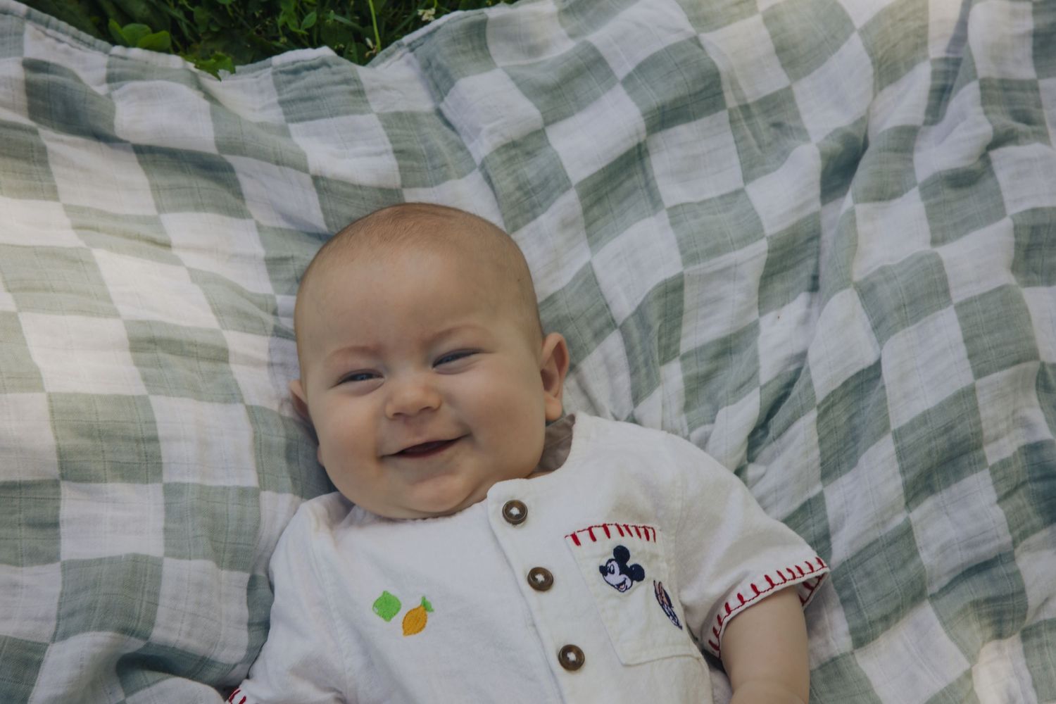 Baby lies on a patterned blanket while smiling happily during a photo session.