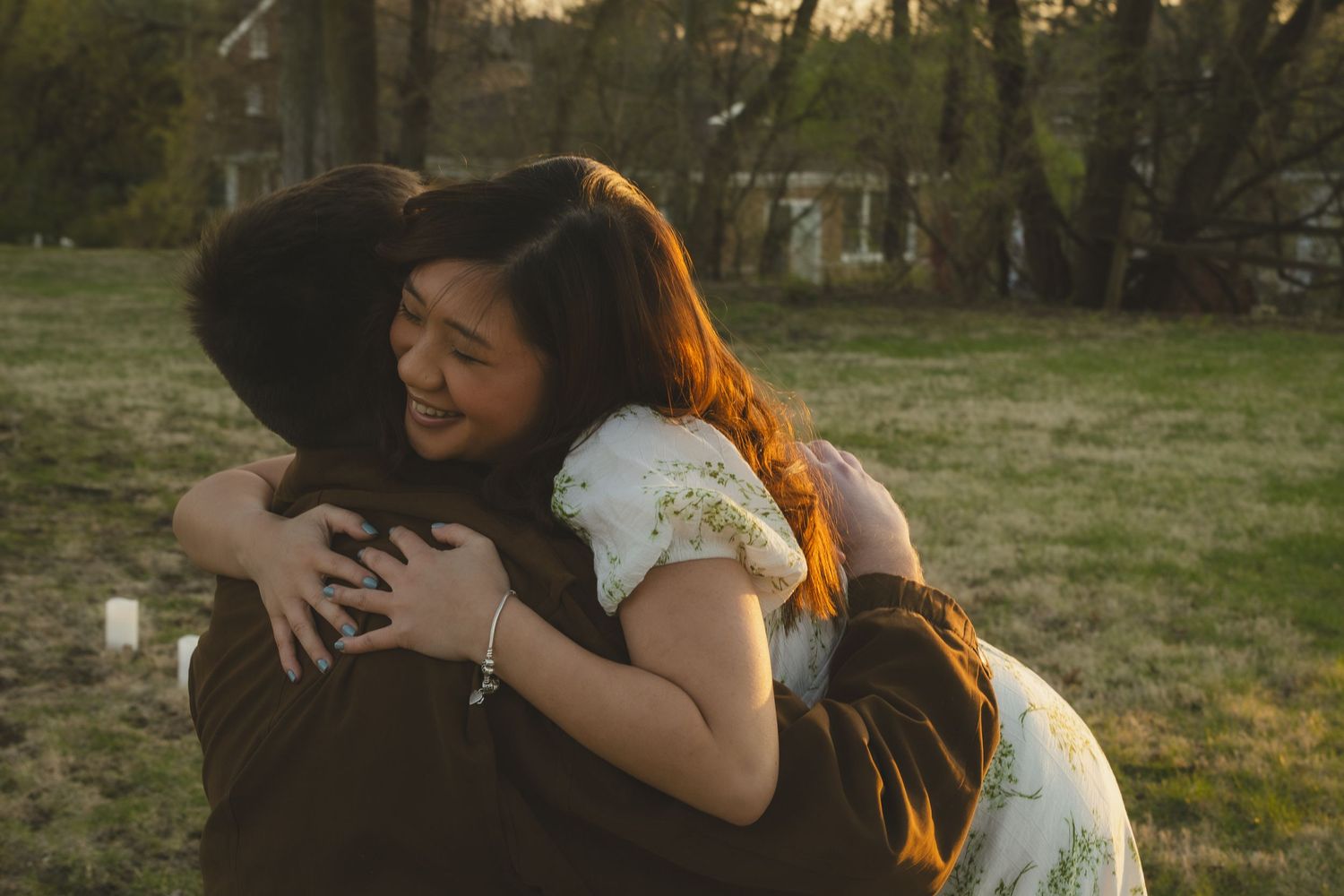 Two people share a warm embrace in golden sunset light on a grassy field.