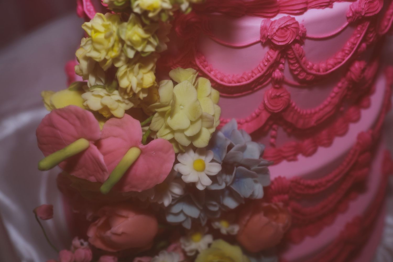 Pink cake decorated with elegant fondant swirls and adorned with yellow, white, and pink floral accents.