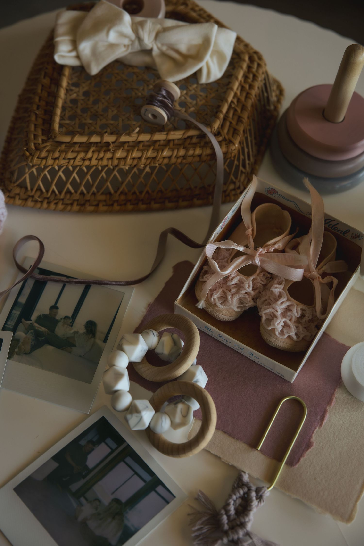 Vintage baby items including woven basket, satin ribbons, tiny shoes, and old photographs arranged in a nostalgic display.