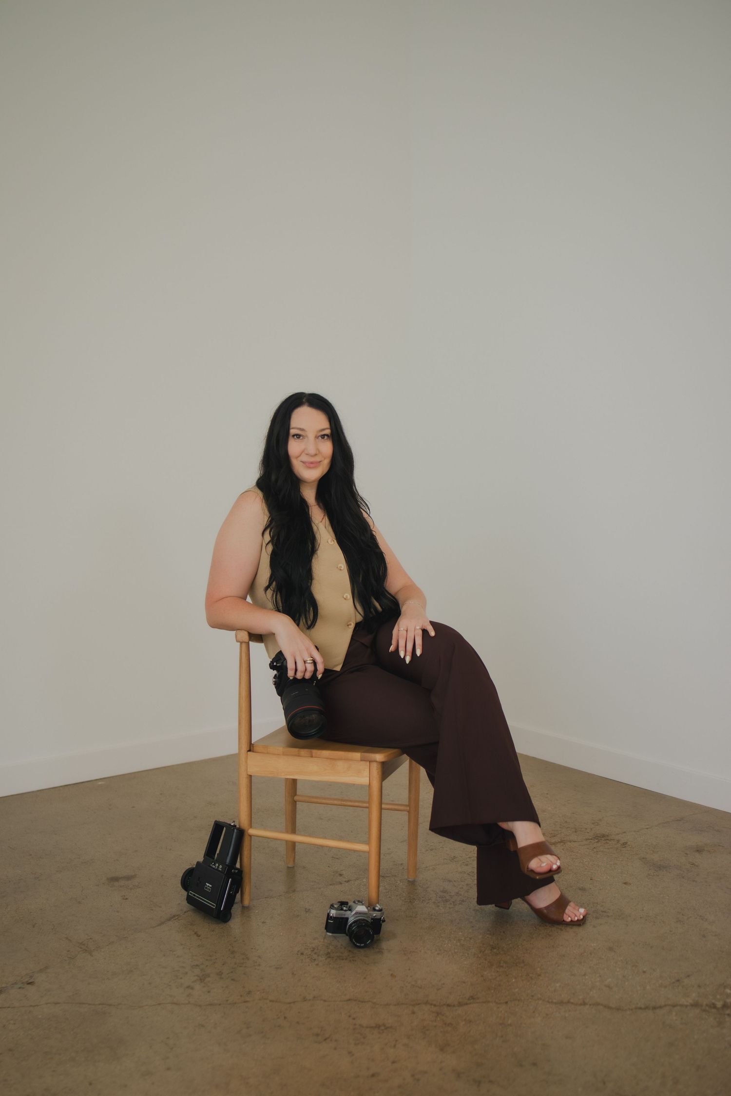 Modern lifestyle portrait against neutral wall with wooden chair, black accessories, and casual brown lounge wear.