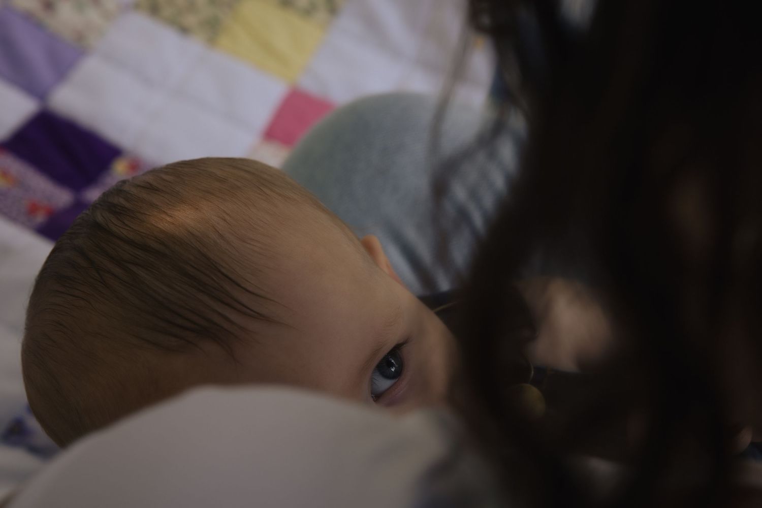 Close-up perspective showing bright blue eyes peeking over bedding or blankets in dimly lit interior.