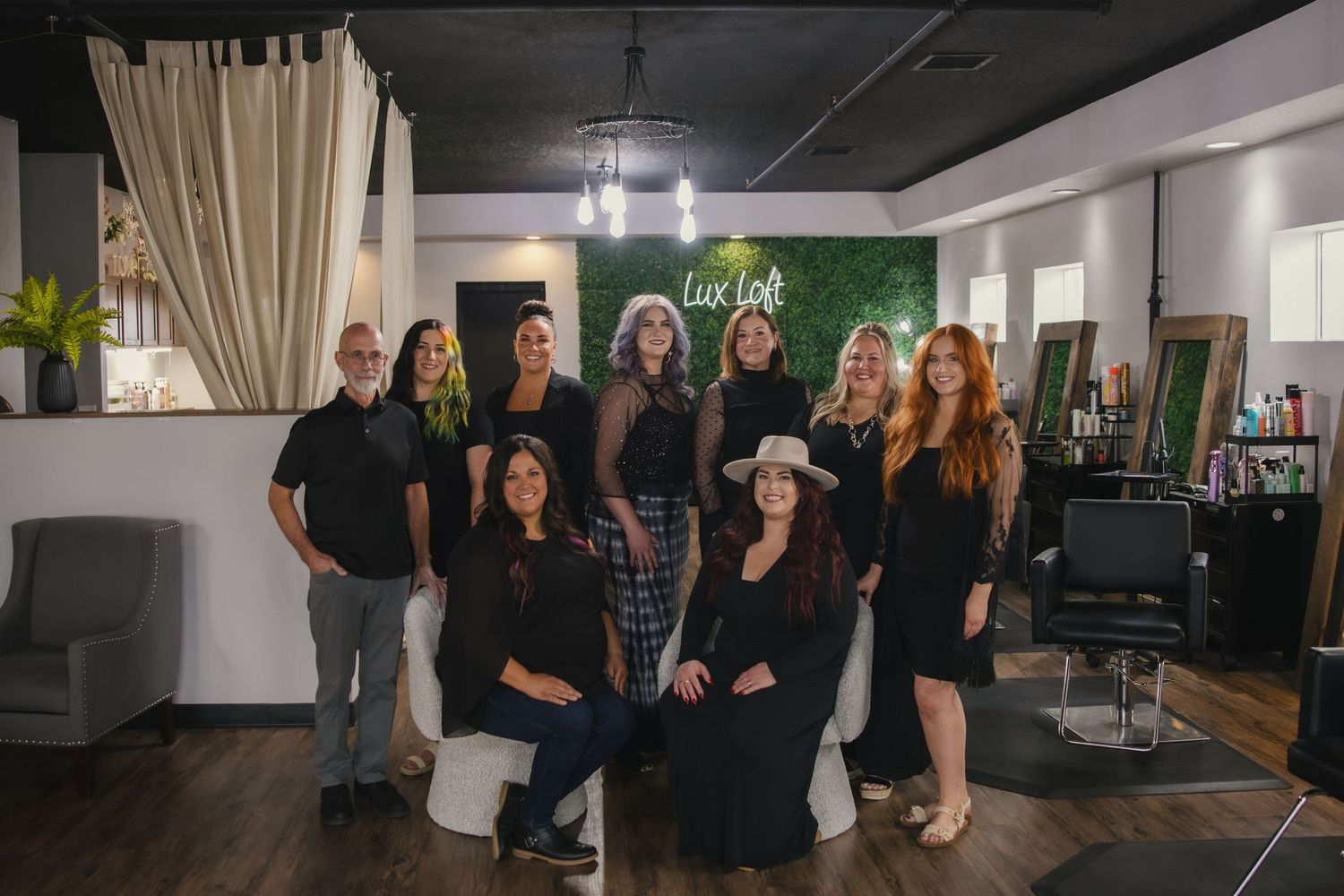 Group of salon professionals posing together inside a modern hair salon with green accent wall and styling stations.