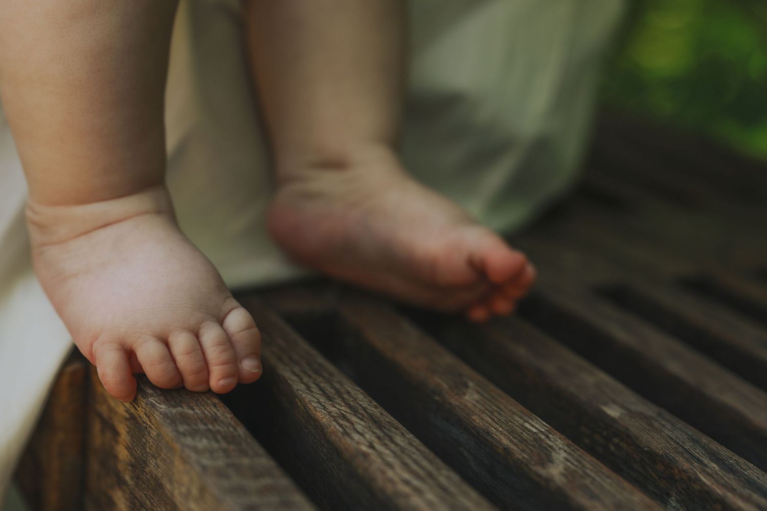 Small chubby baby feet standing on rustic wooden decking in warm sunlight.