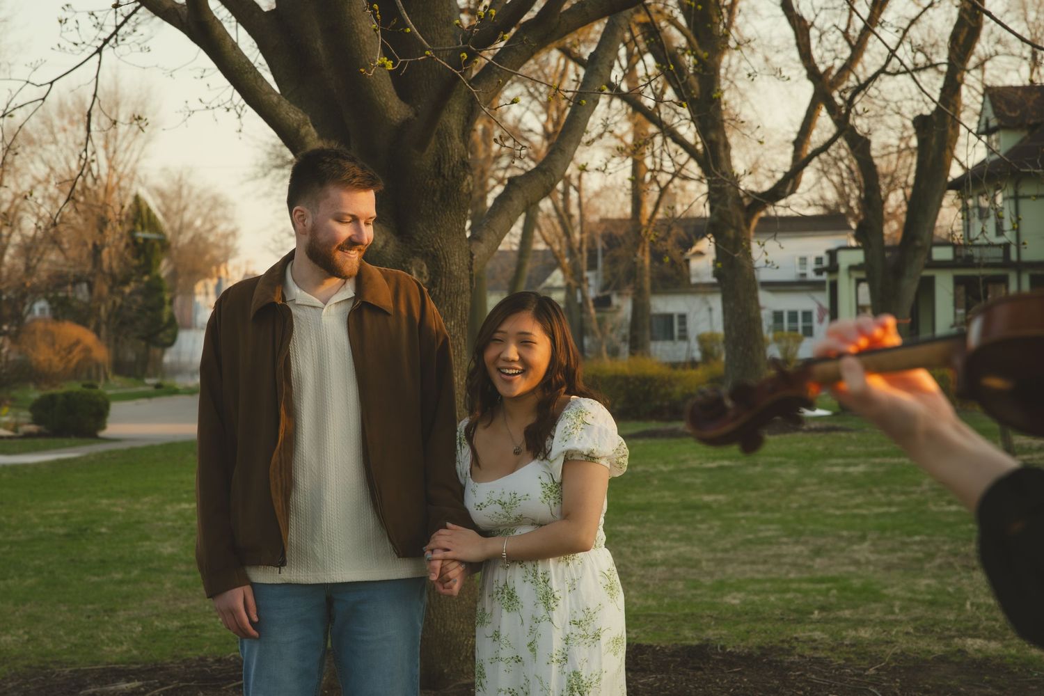 A couple in casual attire holding hands while walking through a park at sunset during a photo session.