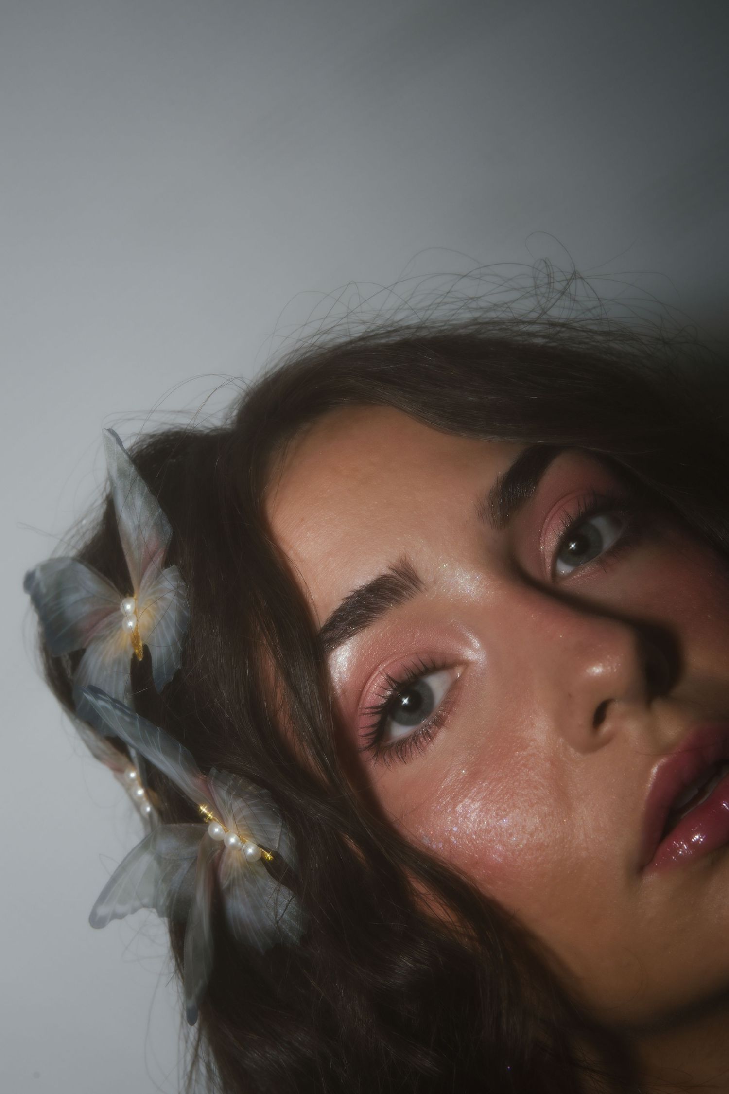 Fashion beauty portrait showing glowy pink makeup look with dramatic lighting and ethereal butterfly hair accessories.