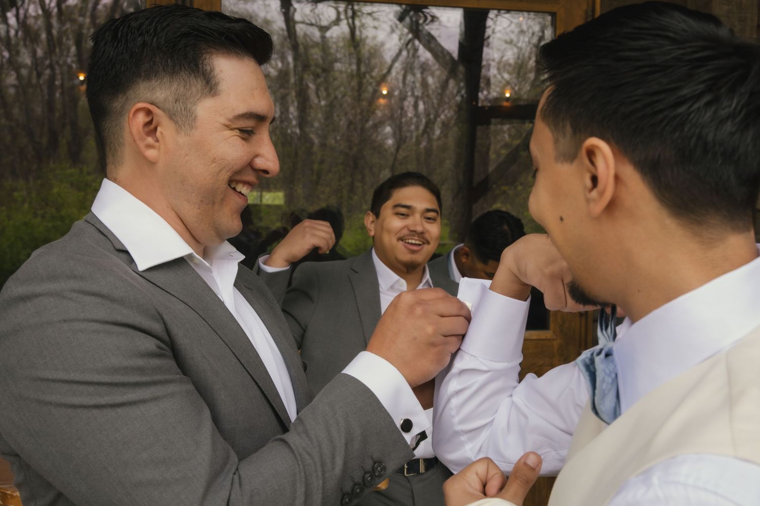 A group of well-dressed men in suits laugh together during a formal outdoor gathering.
