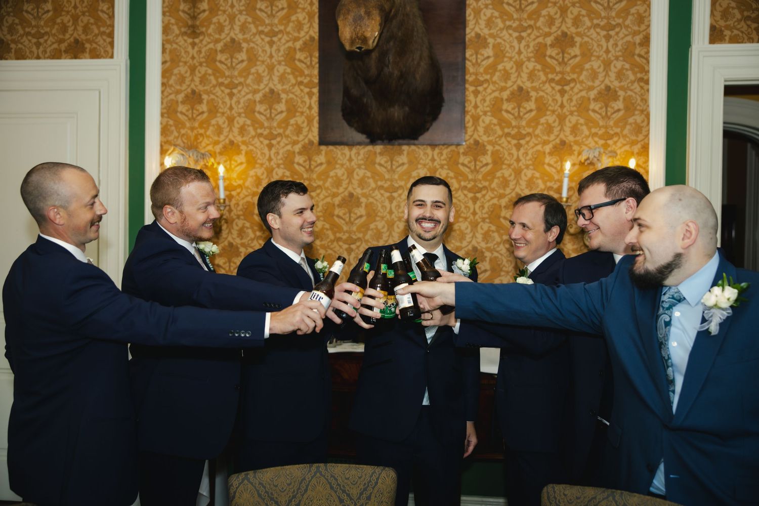 A group gathers at a formal event with patterned wallpaper and toasts with raised glasses in celebration.