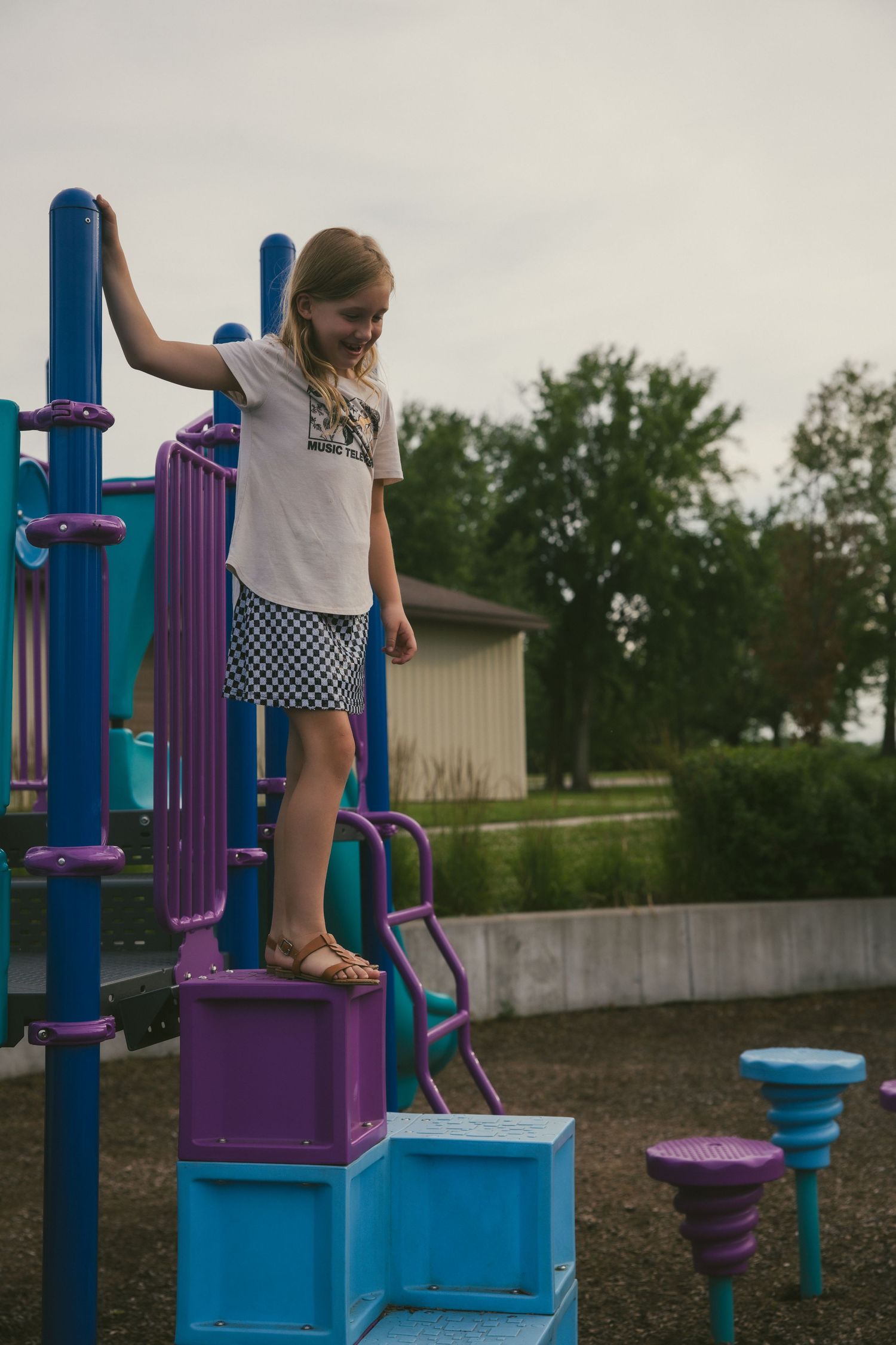 Side view sequence shows child climbing up blue and purple playground equipment at an outdoor park.