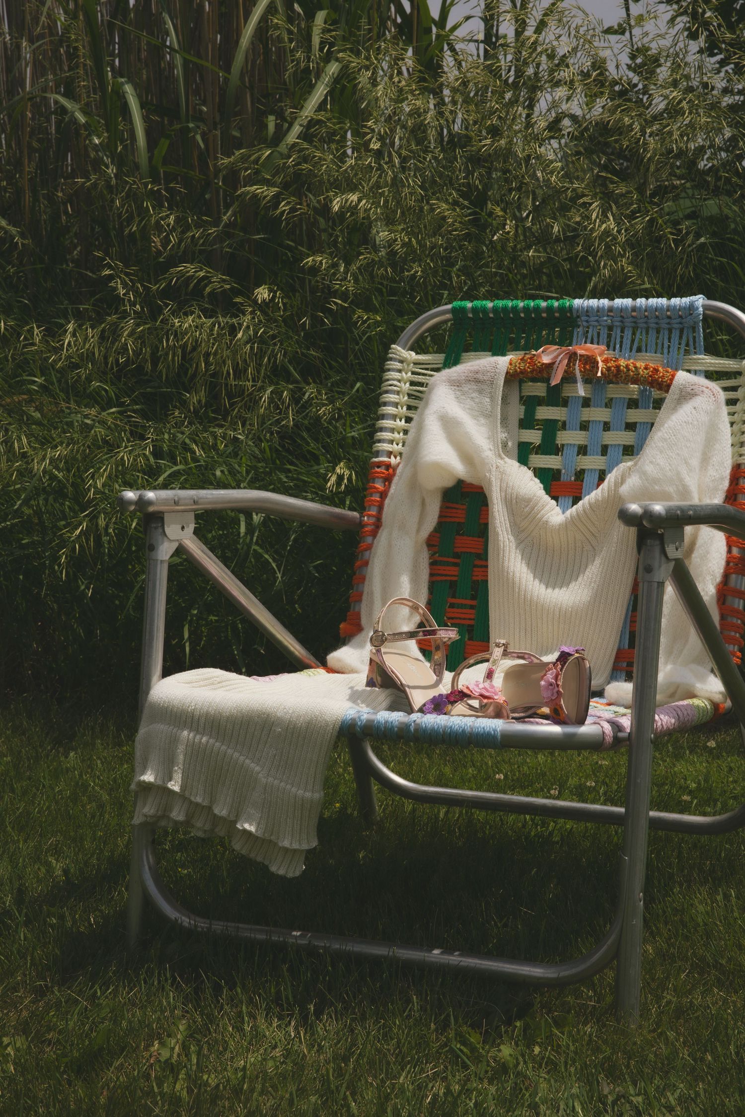 Vintage folding lawn chair with cozy sweater and snacks set up in grassy outdoor setting on sunny day.