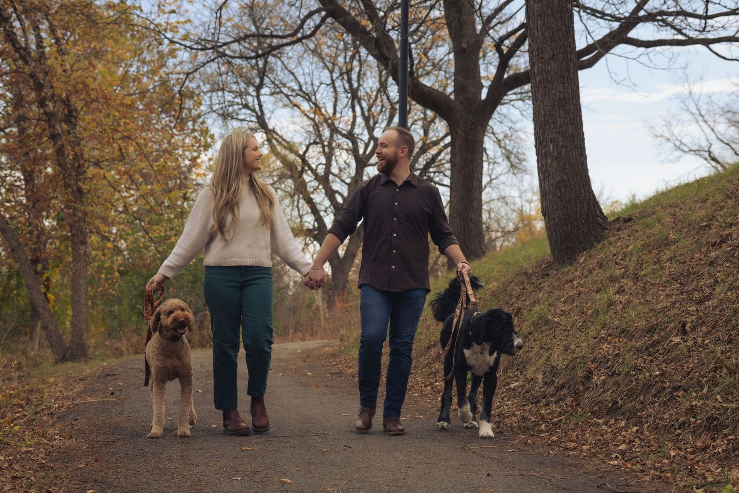 Couple walking dogs on an autumn trail surrounded by fall foliage.
