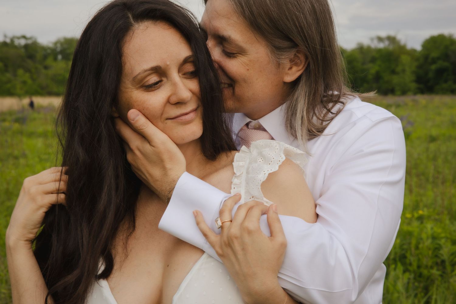 Two people in white embrace tenderly in a green meadow on a summer afternoon.