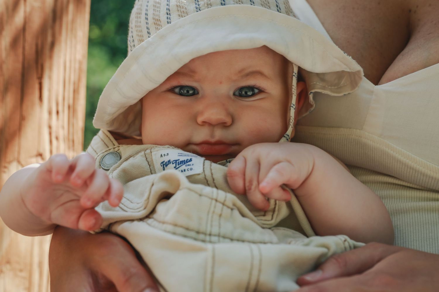 A newborn baby wearing a cream-colored hat and outfit lies swaddled in soft fabric.