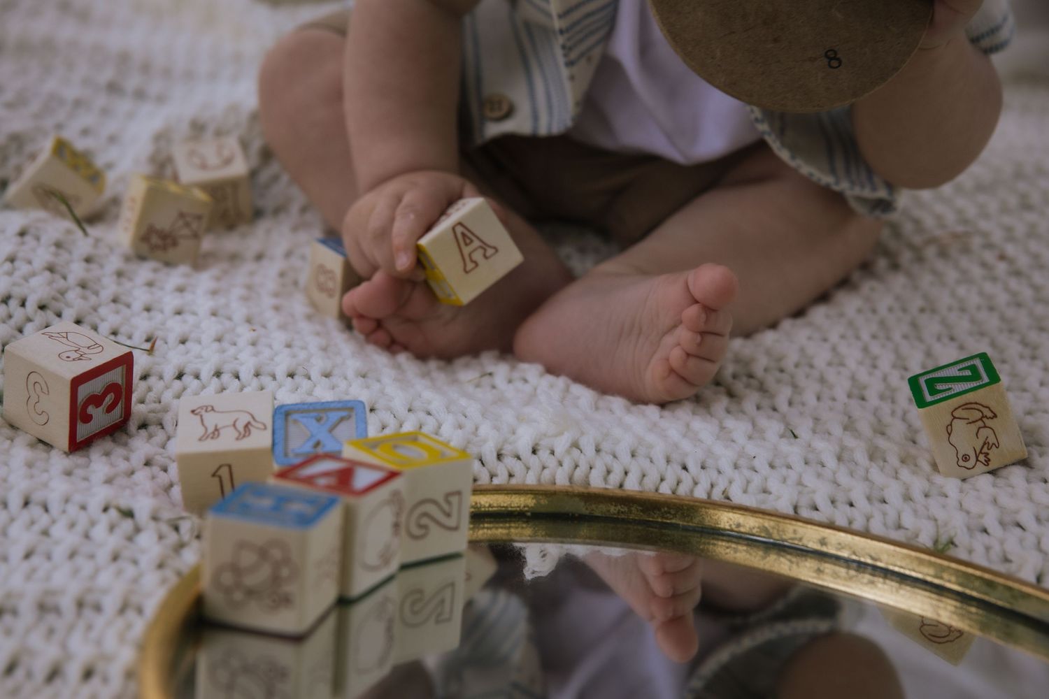 Small feet visible next to wooden alphabet blocks and toy train tracks scattered on a white textured blanket.