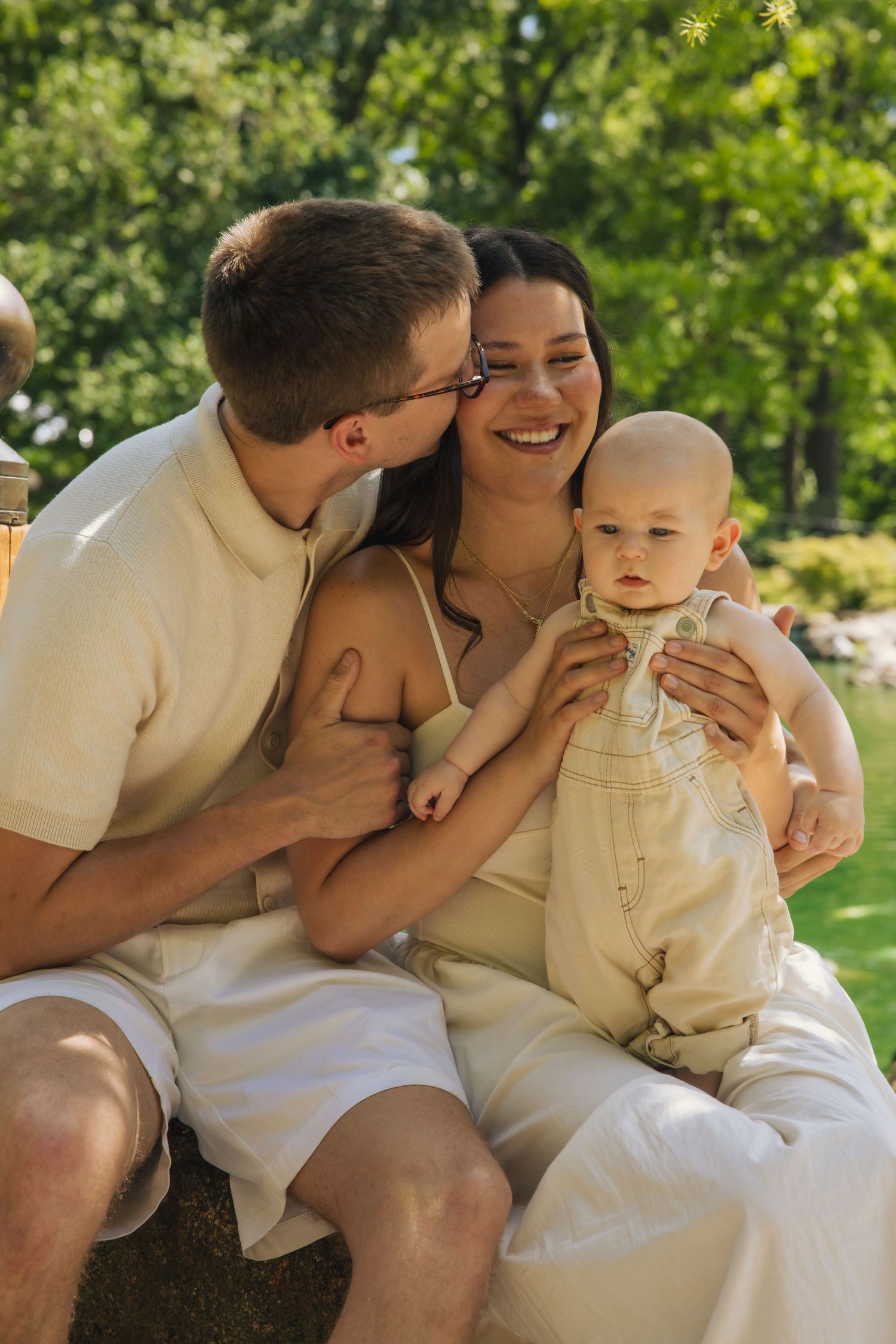 A family sitting together outdoors in light summer clothing sharing a joyful moment in a sunny garden setting.
