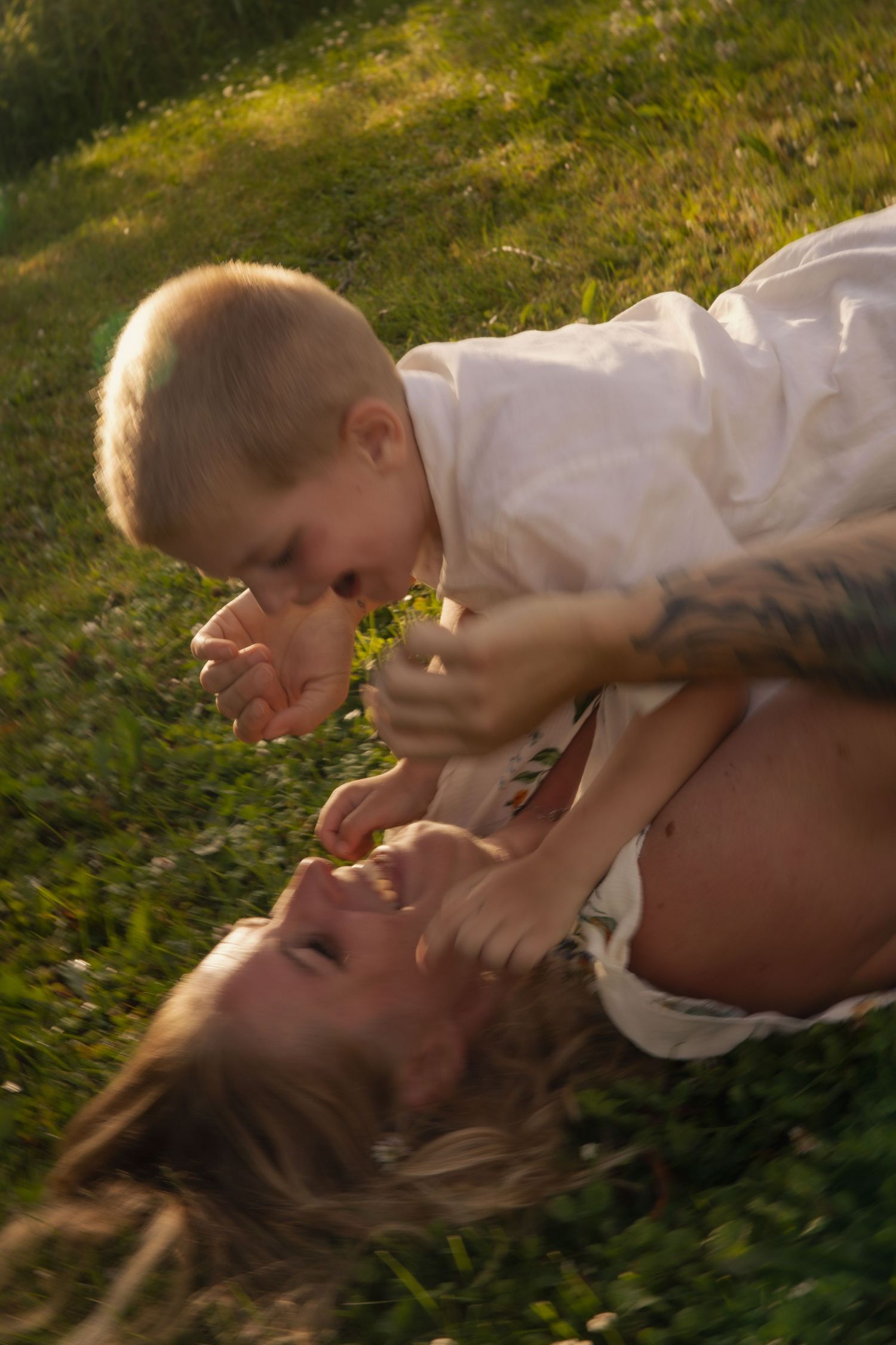 A tender moment shared between two people lying in sunlit grass on a warm day.