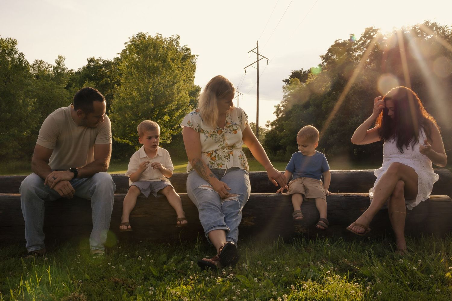 Group of people sitting together on a grassy hill at sunset, creating a peaceful silhouette against the sky.