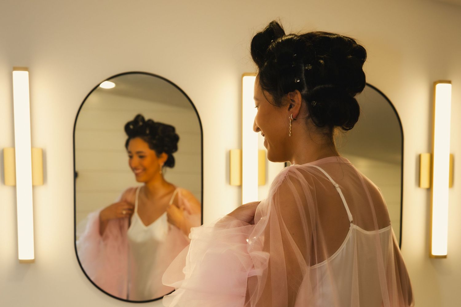 A series of small round bathroom mirrors mounted on a beige wall with vertical light sconces creating a modern aesthetic.