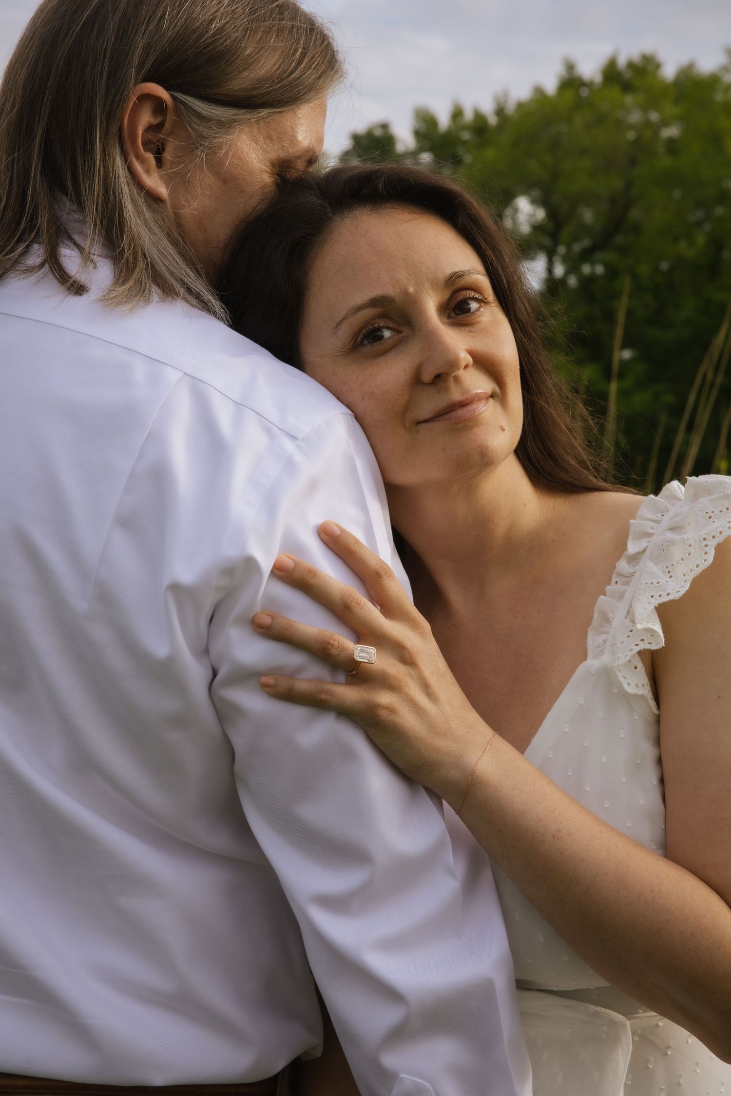 A tender wedding moment captured outdoors as a couple embraces, with a glimpse of greenery in the background.