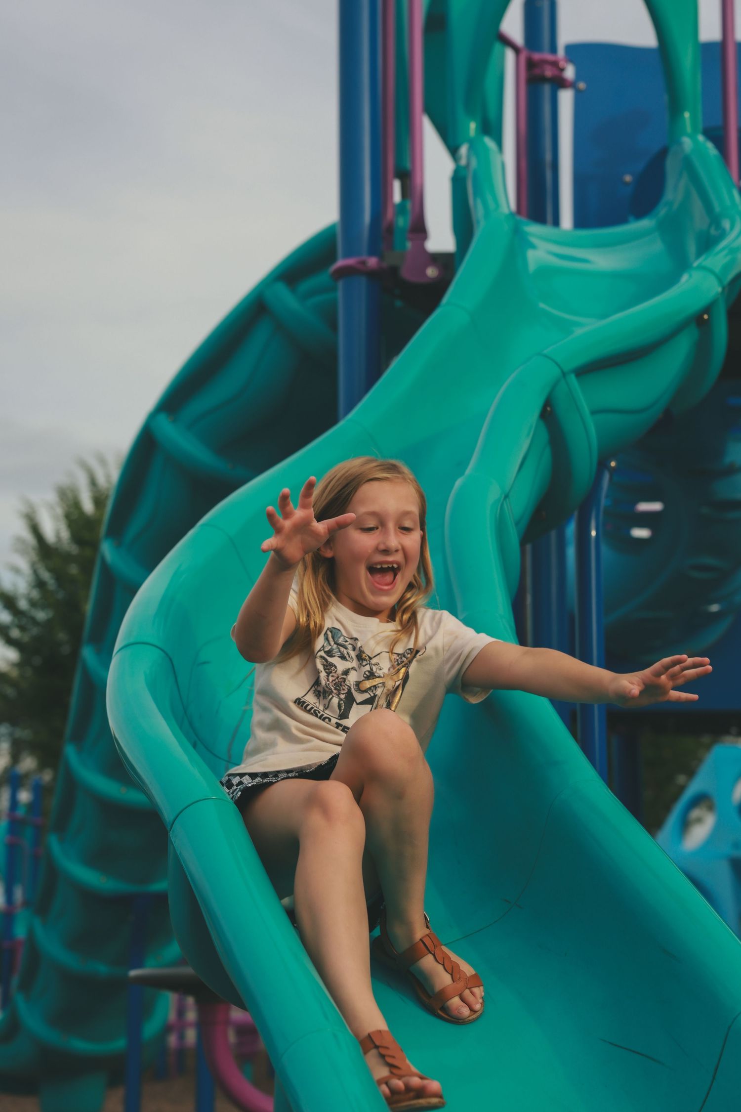 A sequence of four action shots showing someone having fun sliding down a bright turquoise playground slide.