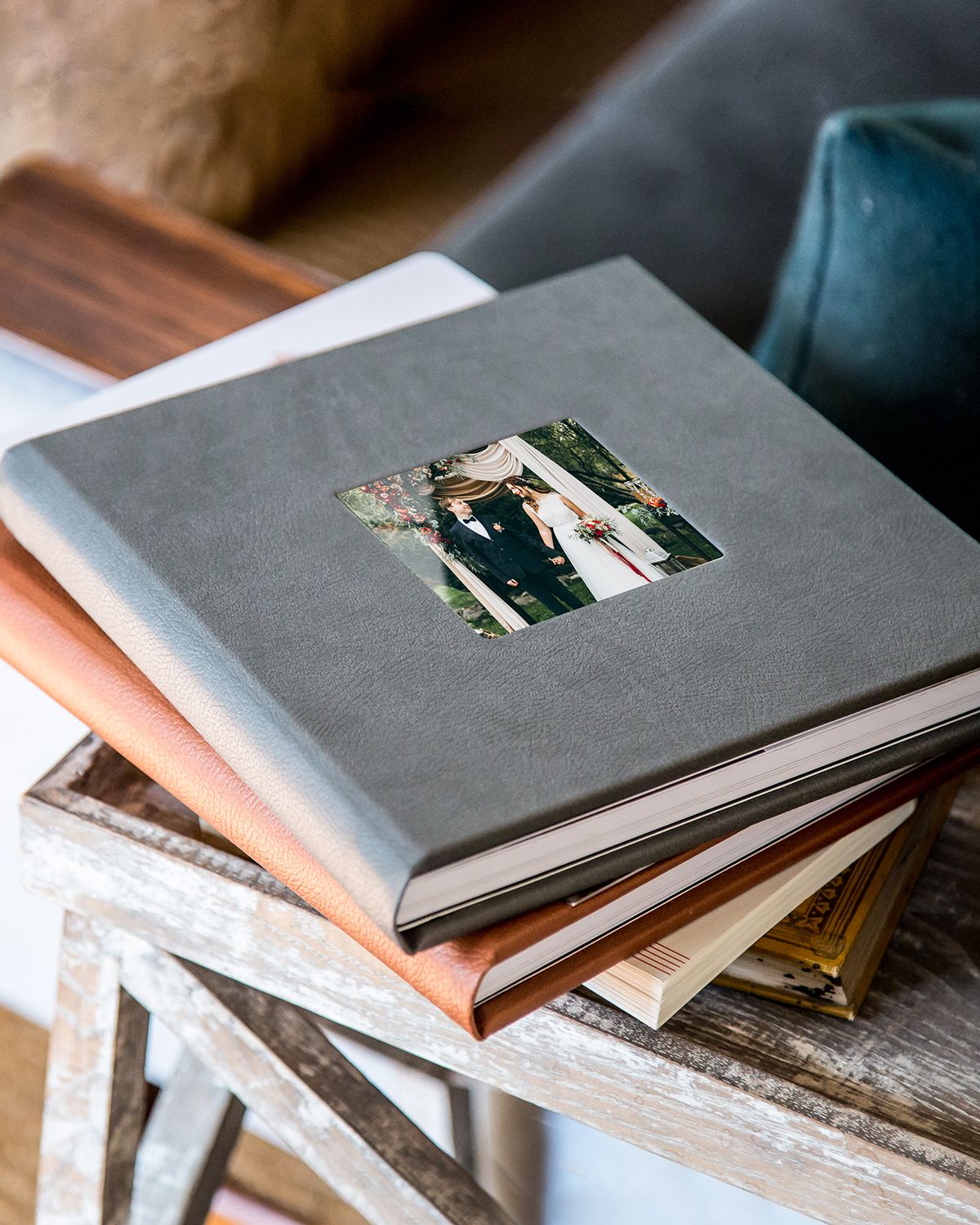 Stack of photo albums with a gray linen cover on top featuring a small window displaying a wedding photograph.