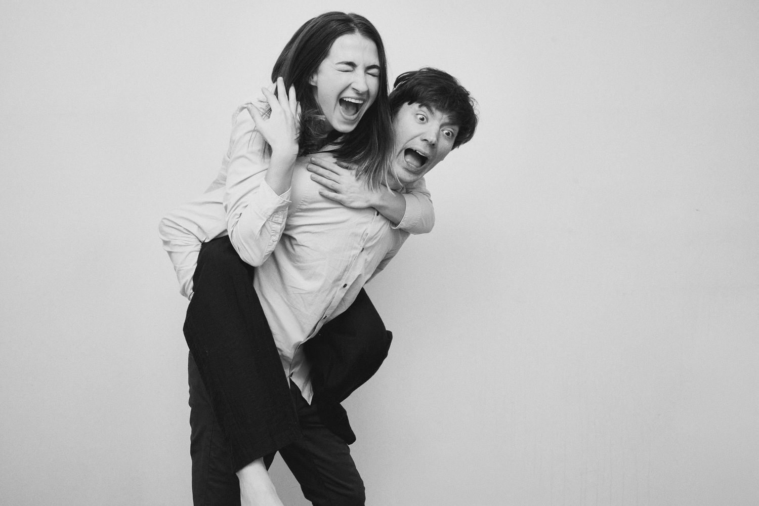 Two people laughing and playing together in black and white against white background.