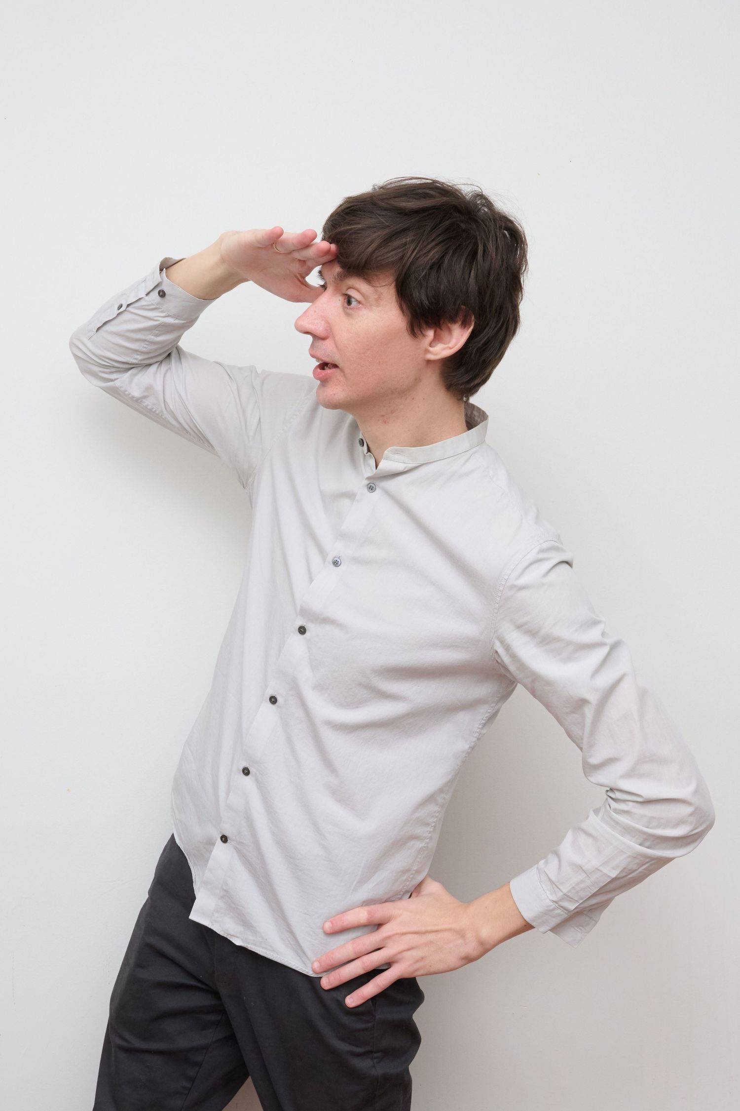 Person in light grey button-down shirt poses dramatically with hand to forehead.