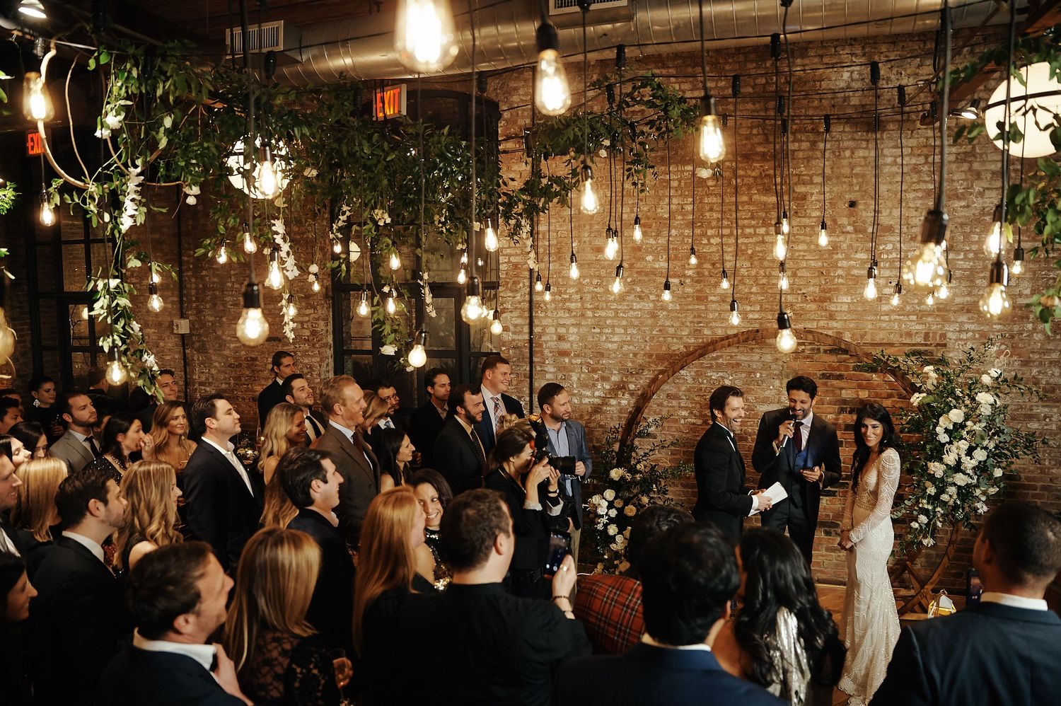 Industrial chic wedding ceremony with hanging lights and exposed brick walls.