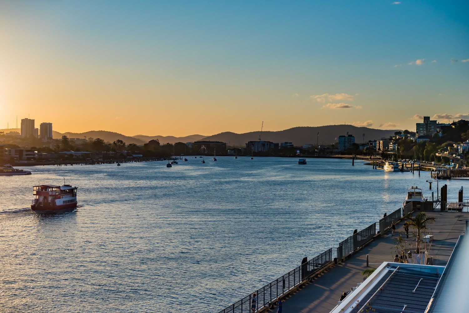 Sunset view of Brisbane River with city skyline and boats in the water.