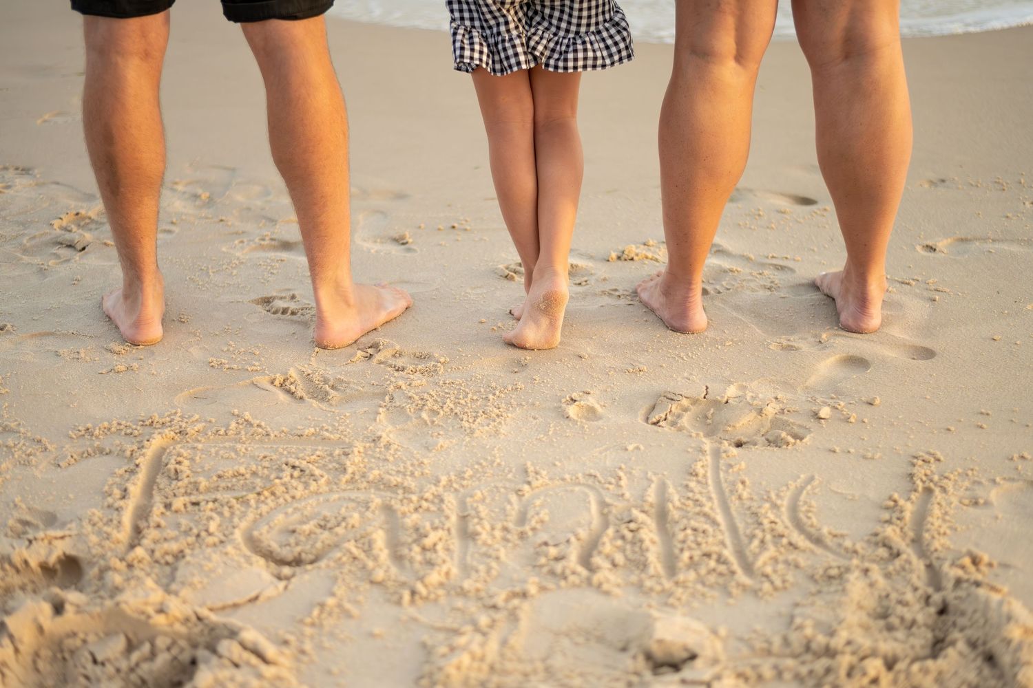Bare feet in sand with family written in beach text during sunset.