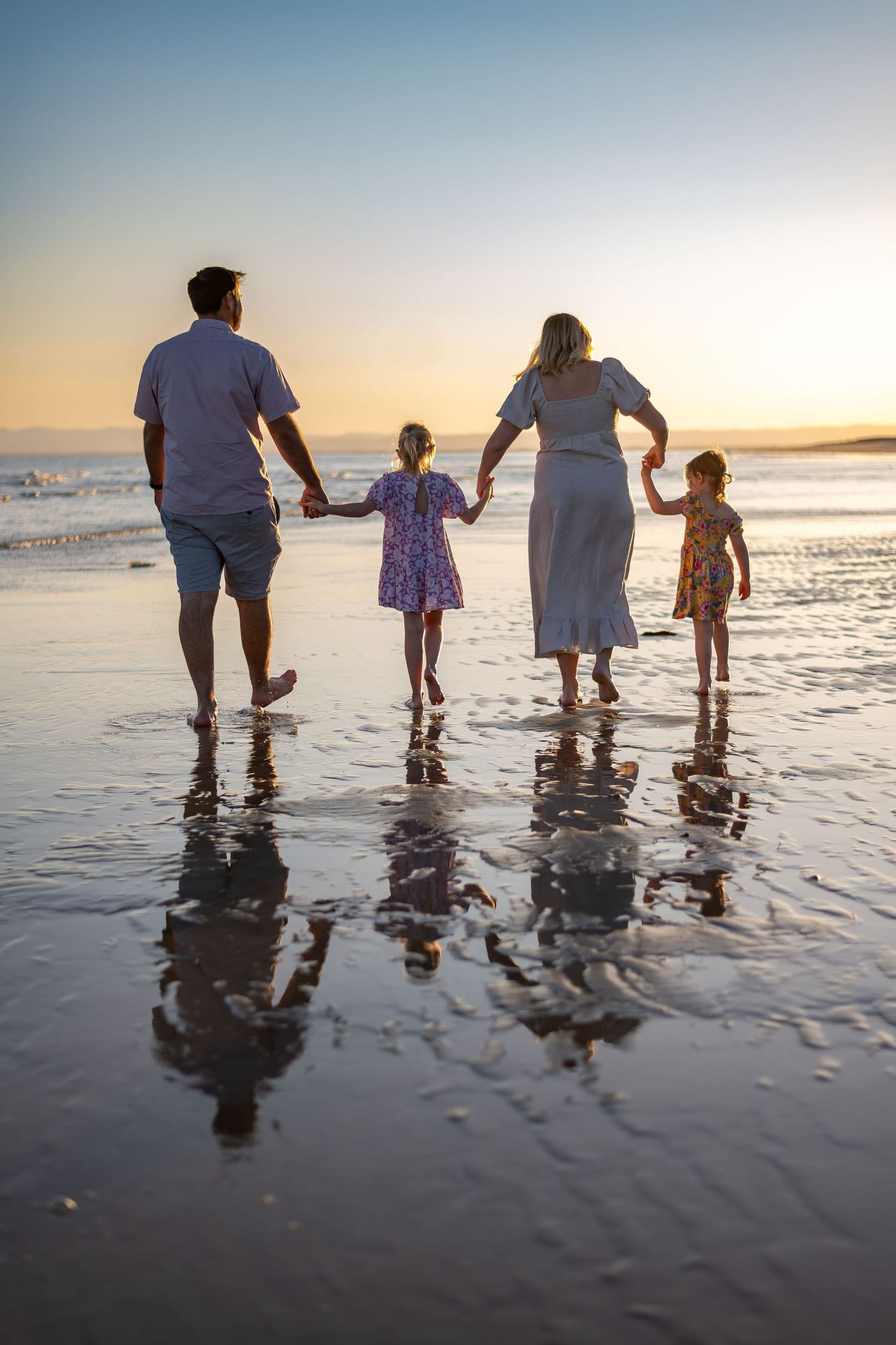Silhouetted family of four holding hands while walking along sunset beach.