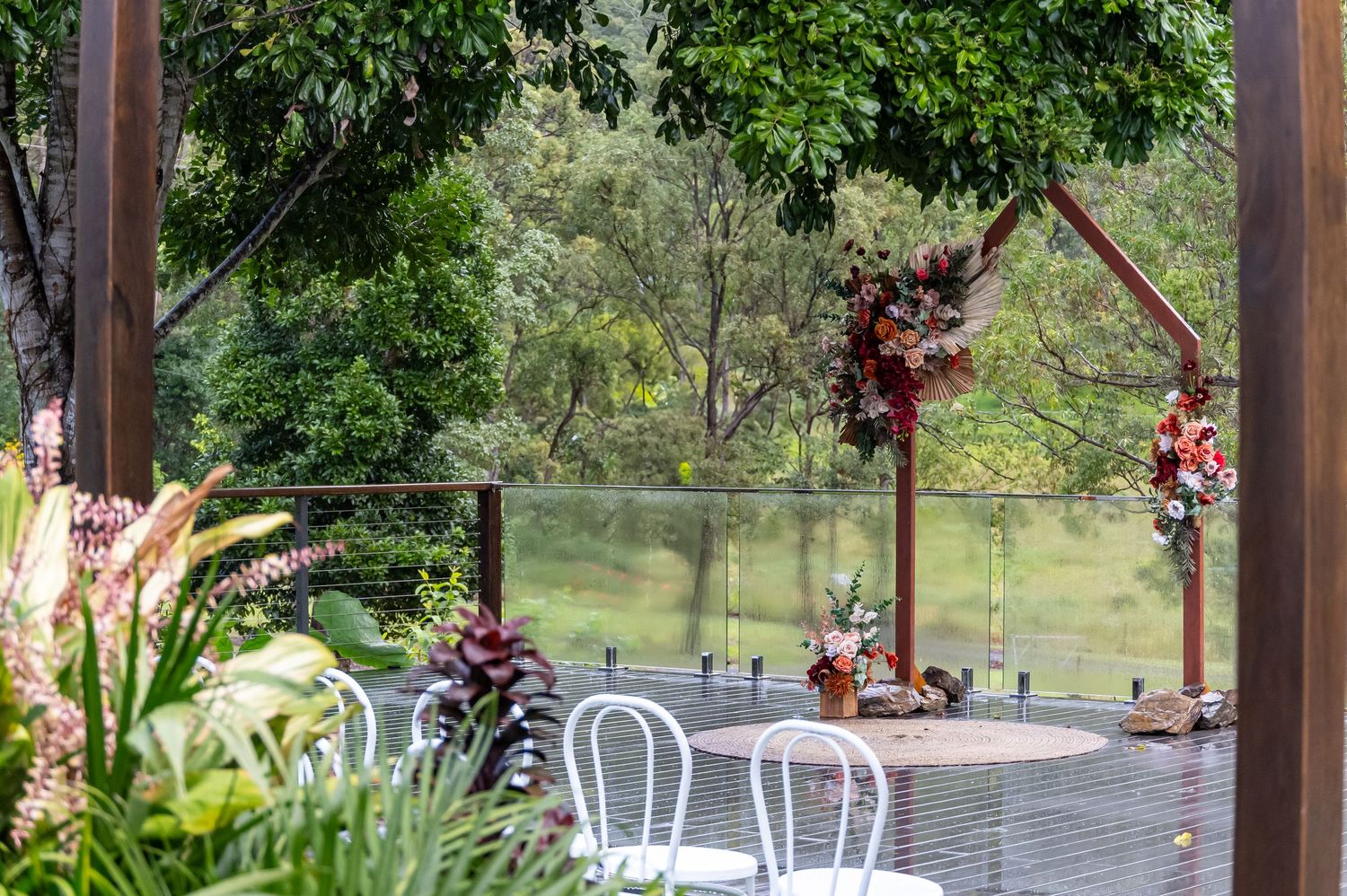Rustic outdoor wedding venue with wooden pergola surrounded by lush greenery and decorative lighting.