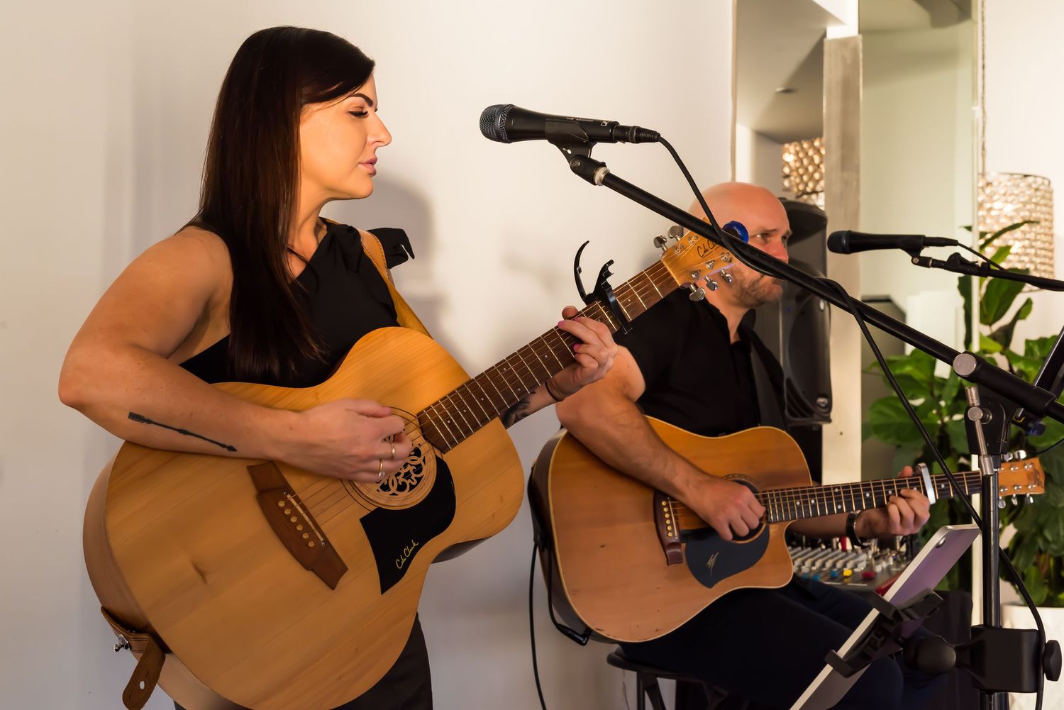 Musicians performing with acoustic guitars and microphones in an indoor setting.