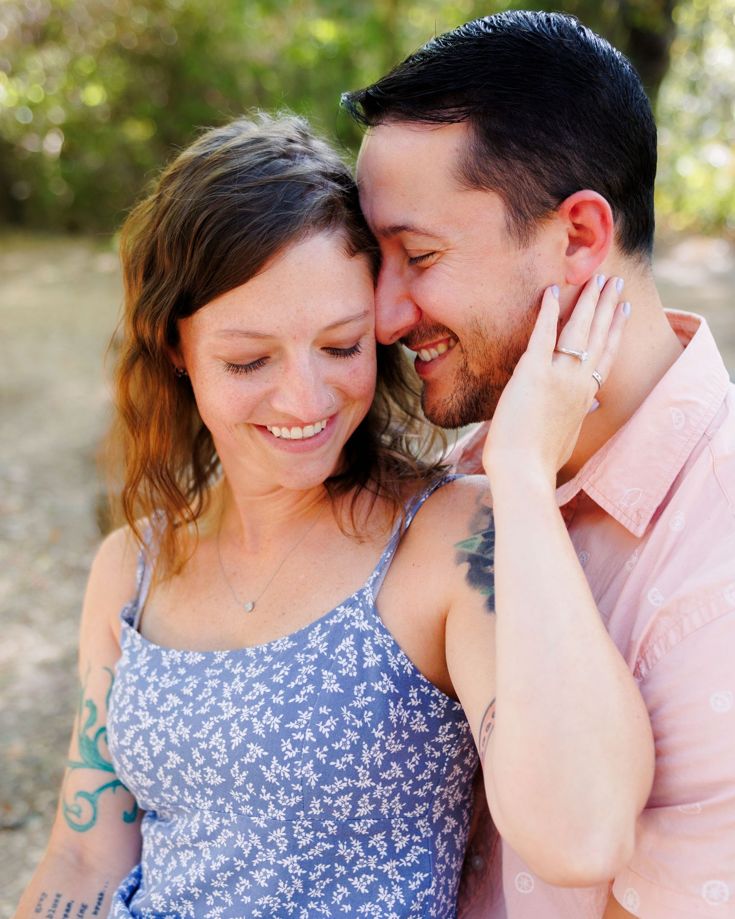 A joyful couple sharing an intimate moment outdoors, with the person in blue floral and pink shirts smiling together.