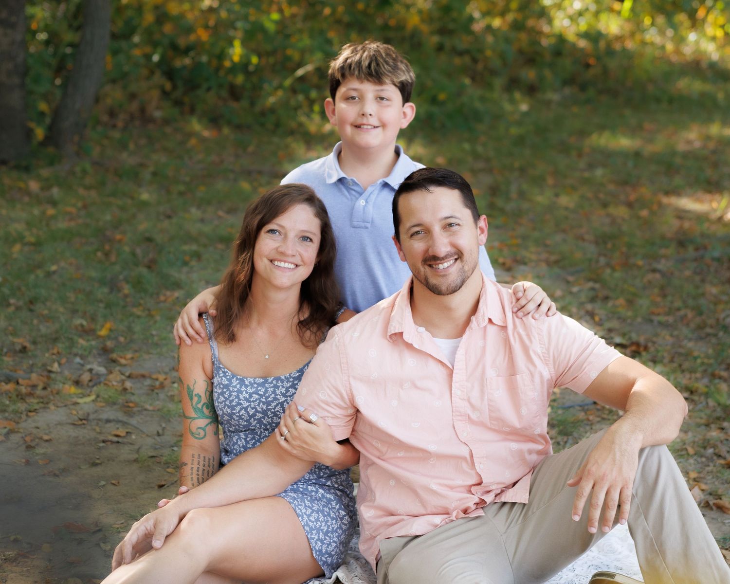 Family portrait captured outdoors in nature showing group of three sitting together on autumn day.
