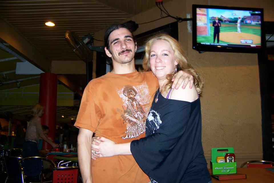 Two people embracing at a casual gathering with a TV showing baseball in the background. Tampa Photographer, Tampa Videographer, Florida