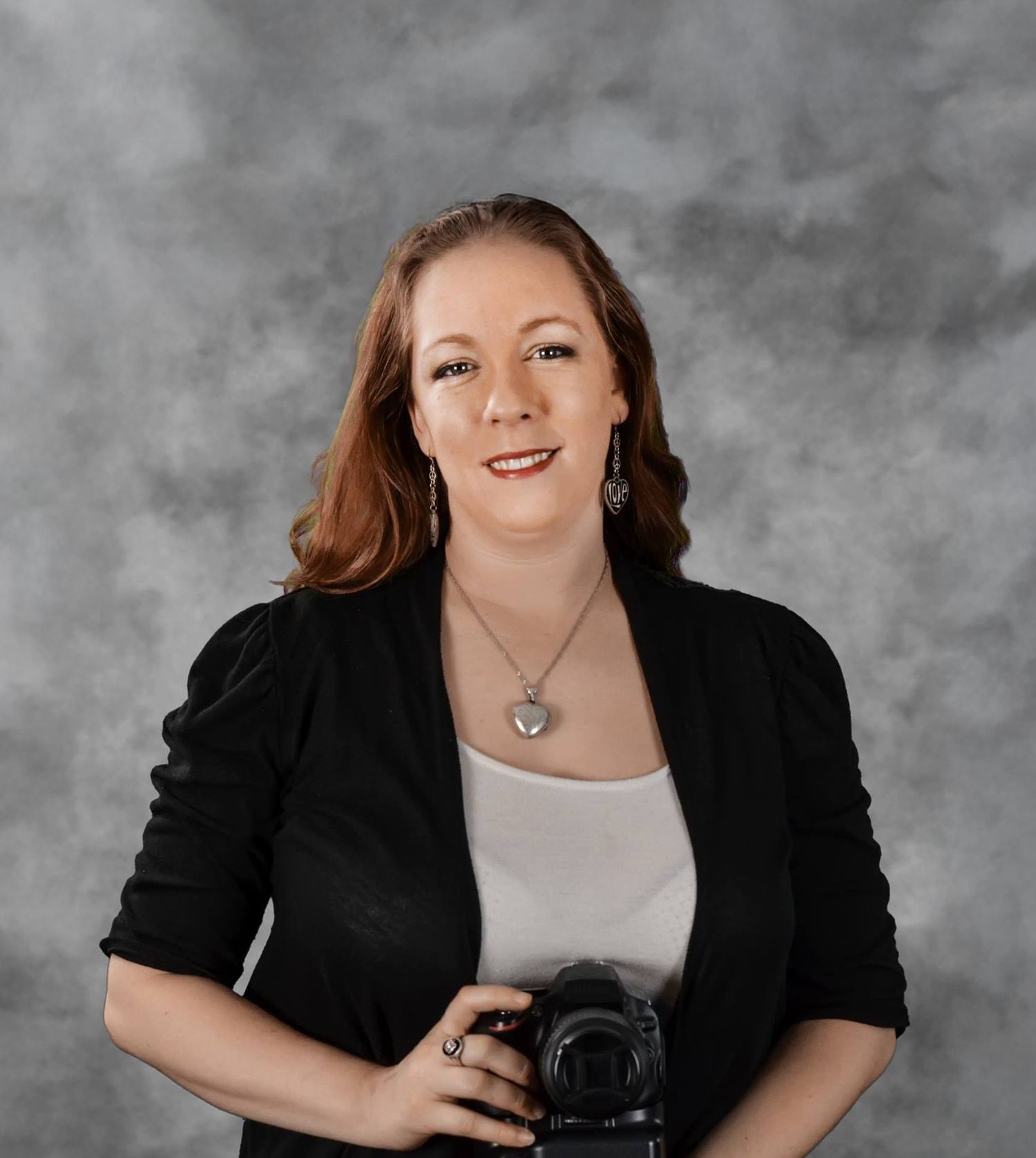 Professional portrait of a photographer wearing a black blazer and white top with a DSLR camera against a gray background. Tampa Photography