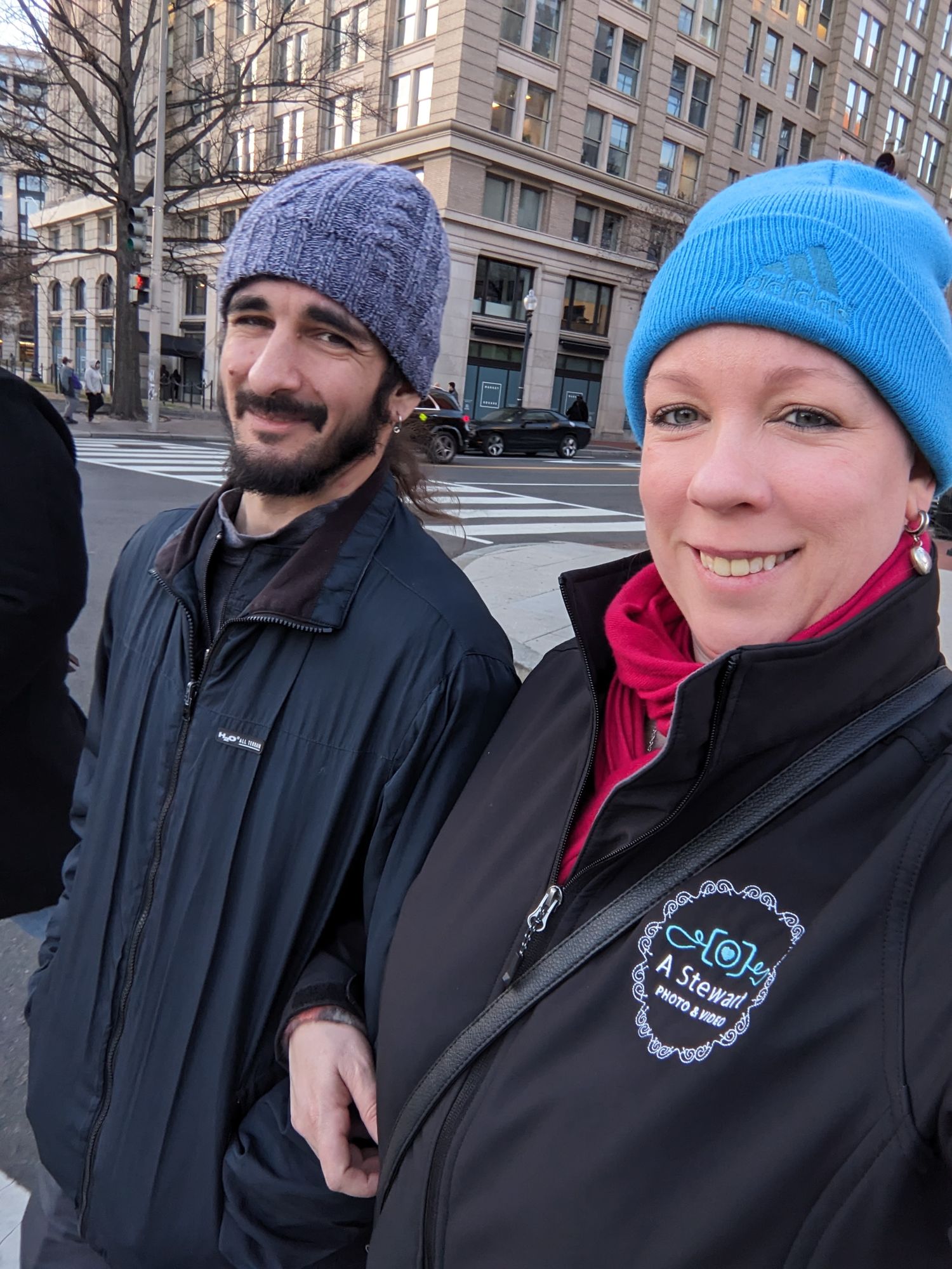 Two people wearing winter hats and jackets stand together on a city street with brick buildings in the background. Tampa Photographer