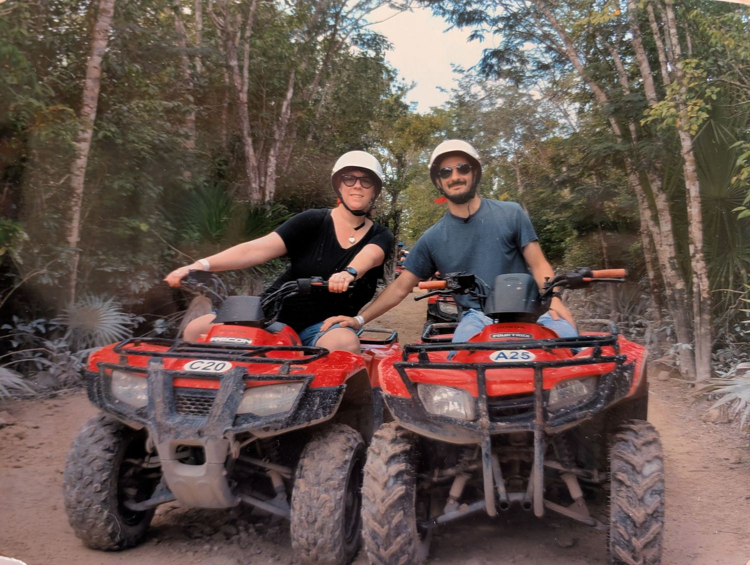 Two people in helmets sit on parked red ATVs on a wooded trail during a recreational outdoor adventure. Tampa Photographer