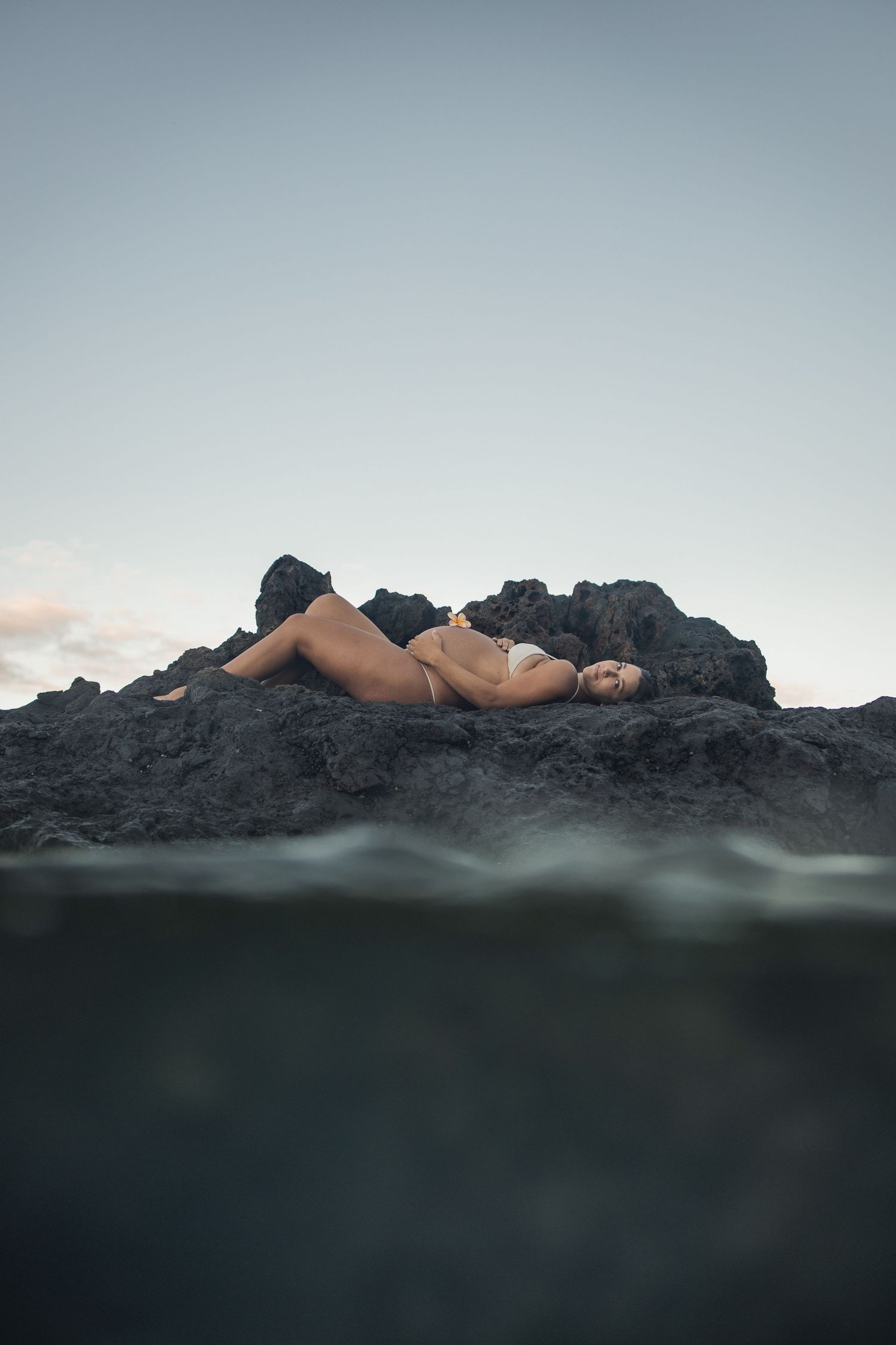 pregnant woman laying on lava rocks above water on Maui beach