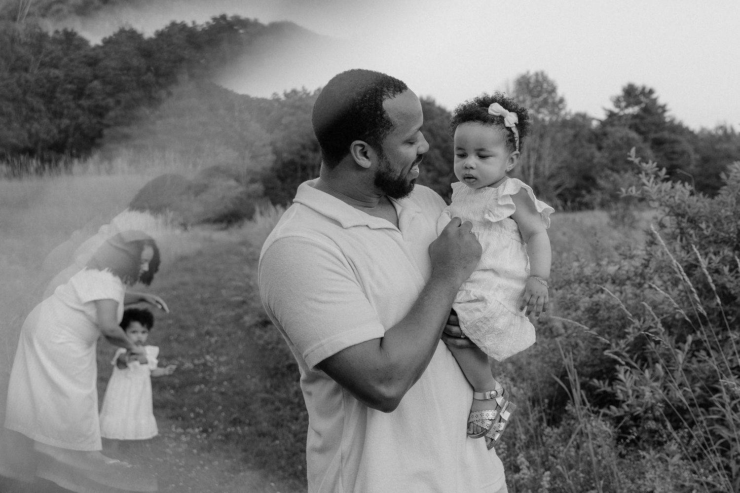 A tender black and white family moment outdoors in a misty natural setting with soft morning light.