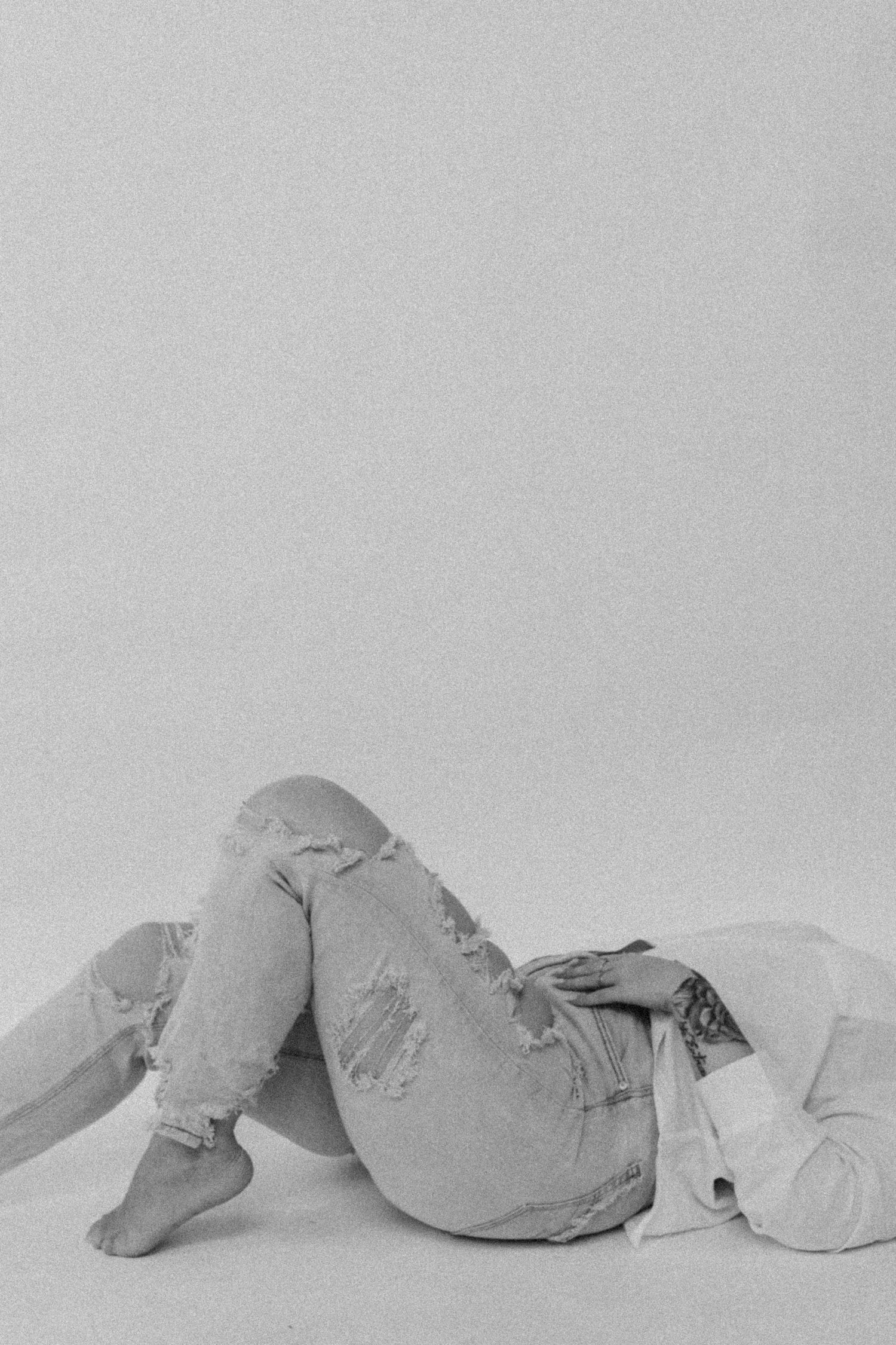 Minimalist black and white photo of relaxed person in denim lying down against plain background.